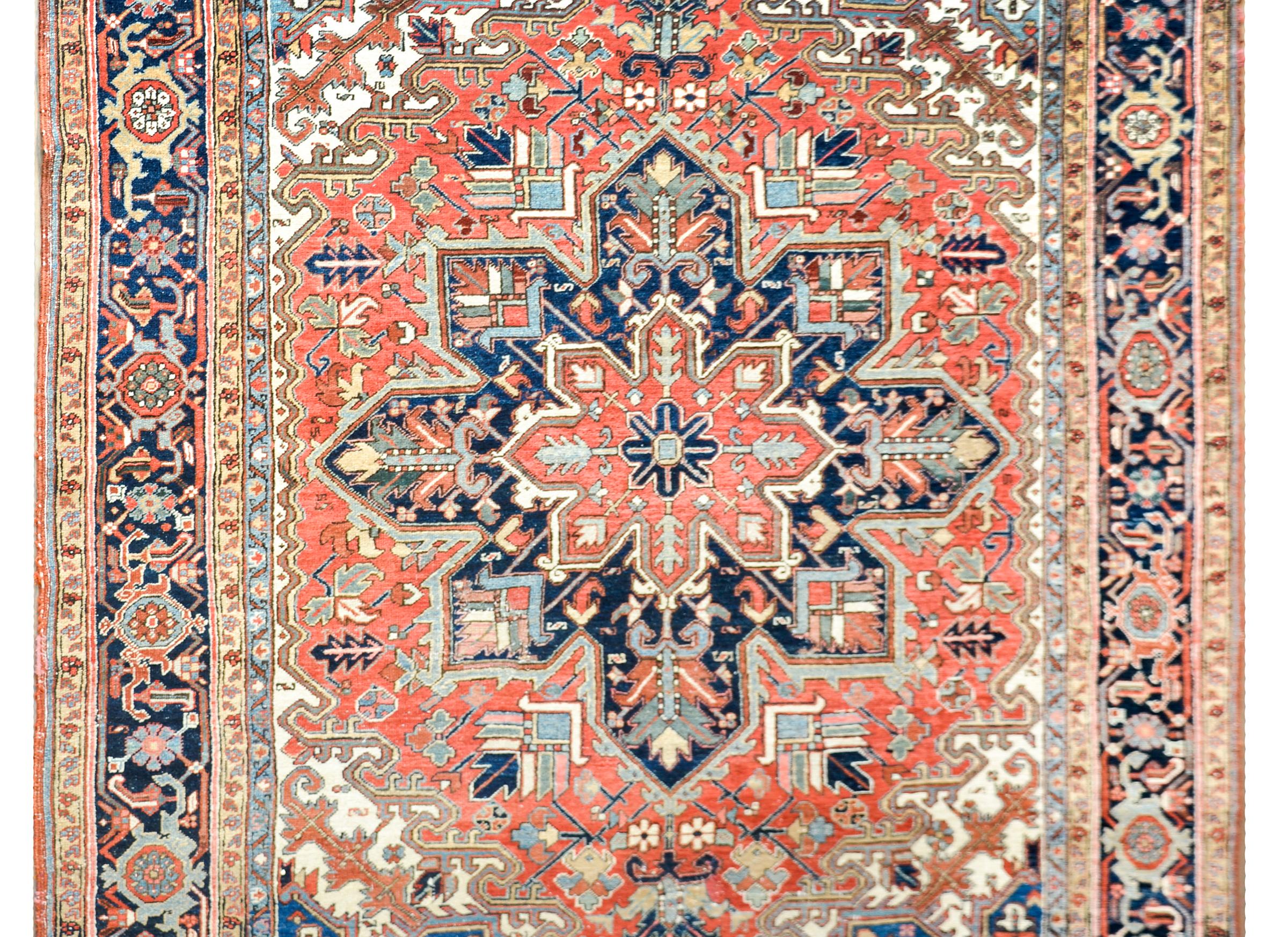 An incredible early 20th century Persian Heriz rug with a traditionally woven stylized floral pattern containing a large central medallion amidst a field of elaborately woven scrolling vines and flowers, all woven in crimson, cream, light and dark