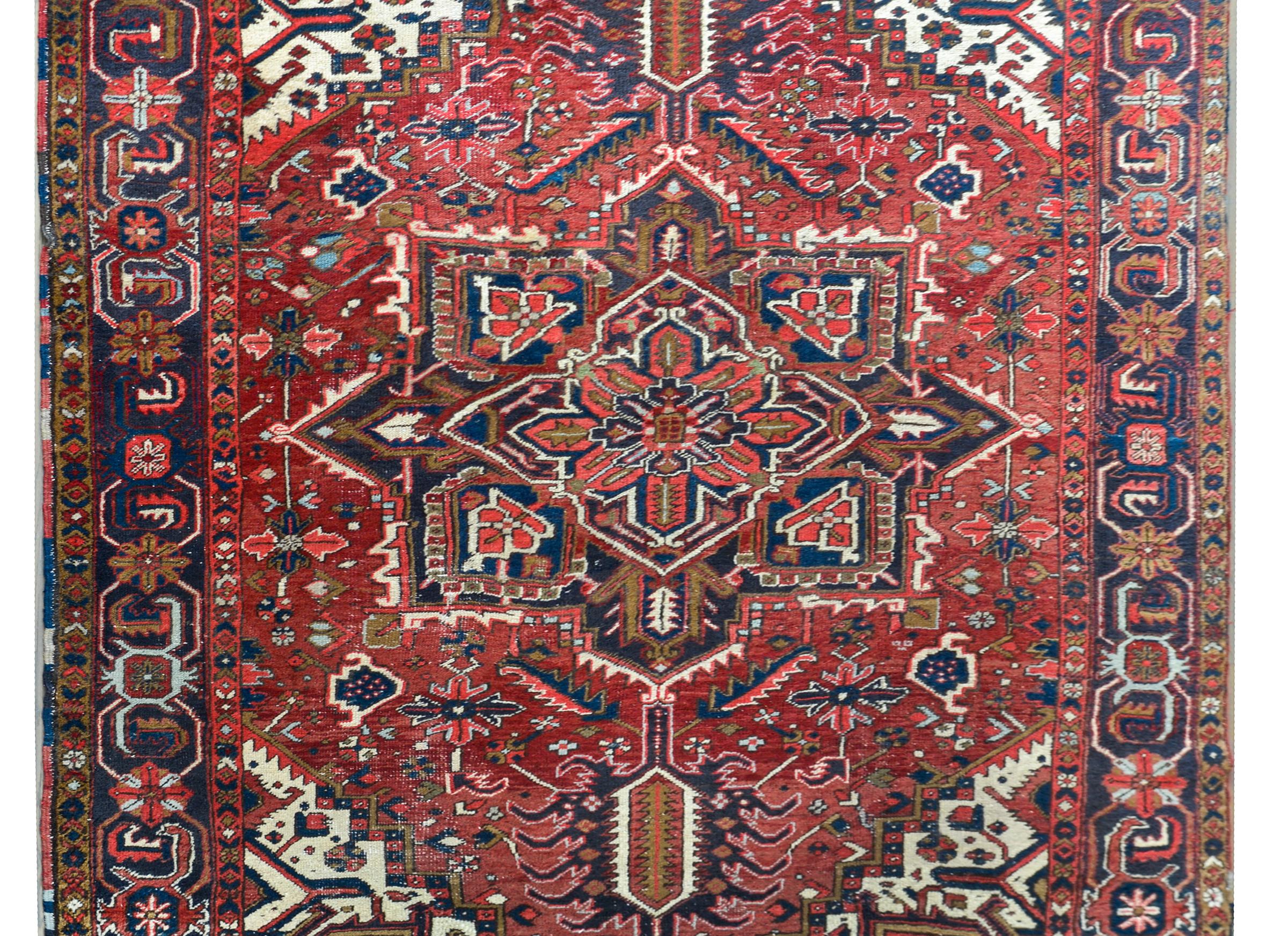 A striking early 20th century Persian Heriz rug with a large central eight-lobed floral medallion woven in myriad colors including coral, indigo, brown, pink, and white, and living amidst a field of more stylized flowers. The border is wonderful