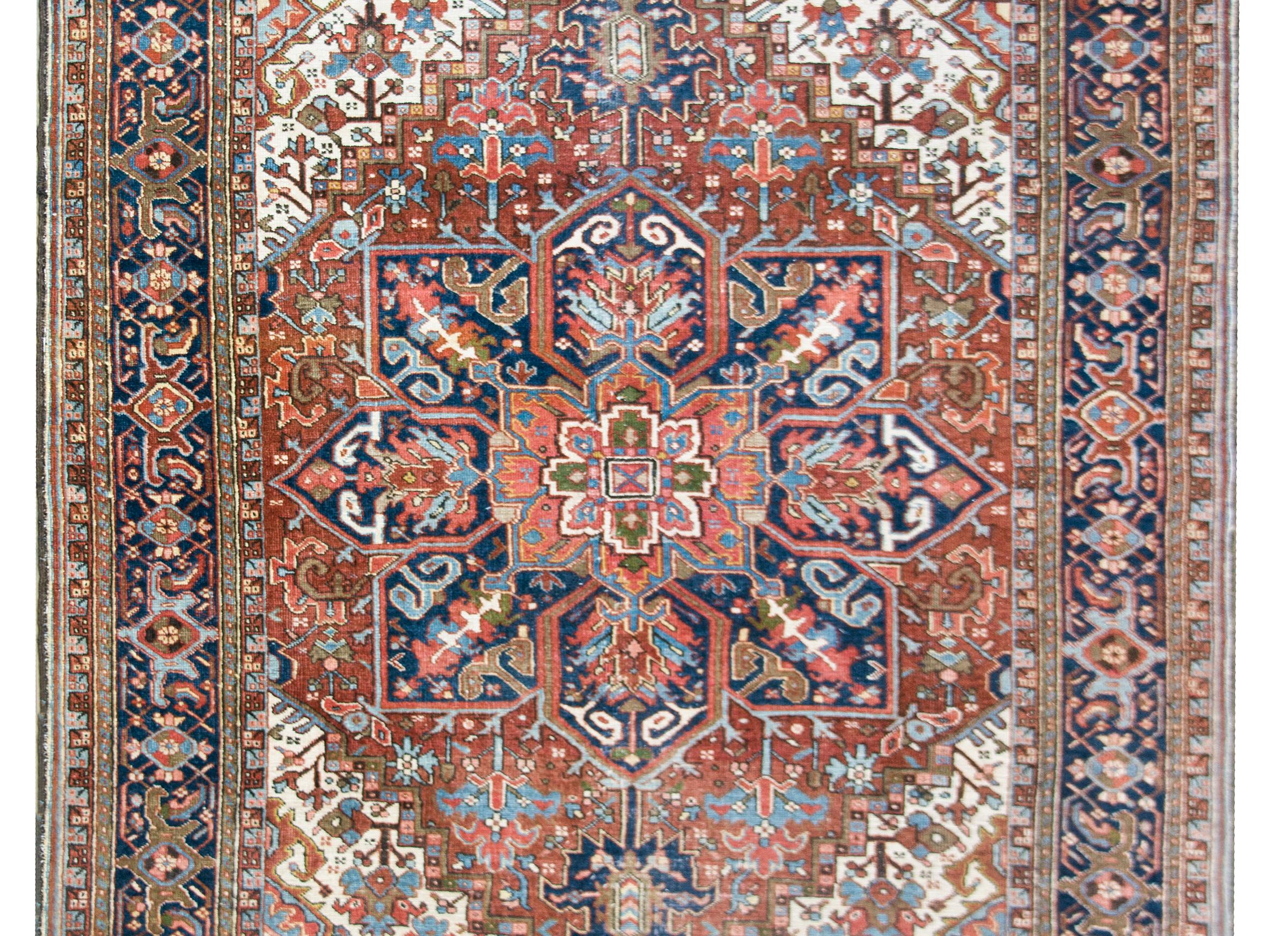 A bold early 20th century Persian Heriz rug with a traditional large central floral patterned medallion woven in myriad colors including crimson, indigo, green, pink, and white, and set against a crimson background. The border is stunning comprised