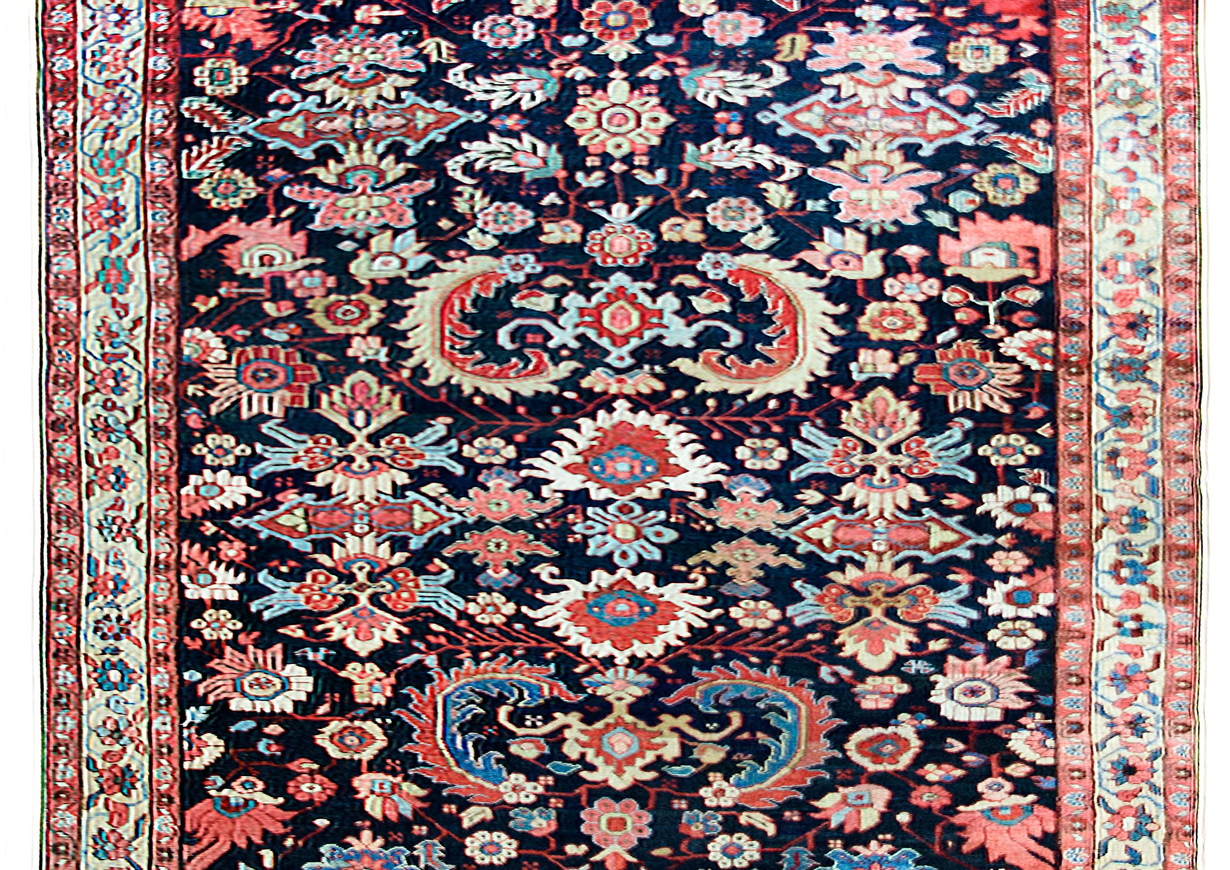 A stunning early 20th century Persian Heriz rug with an all-over mirrored floral pattern with myriad stylized large-scale flowers and leaves woven in crimson, pink, light and dark indigo, cream and brown, and set against a dark indigo background. 
