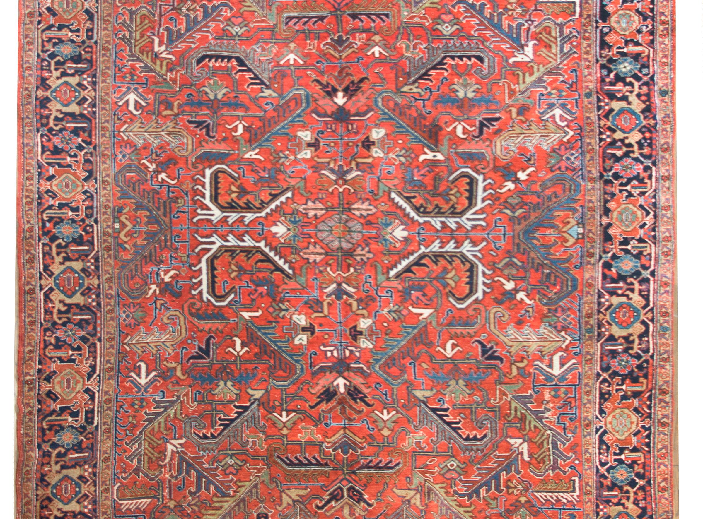 A wonderful early 20th century Persian Heriz rug with a large-scale mirrored floral and leaf pattern woven in tradition Heriz colors of crimson, light and dark indigo, white, pink and cream, and surrounded by a fantastic border with a wide central