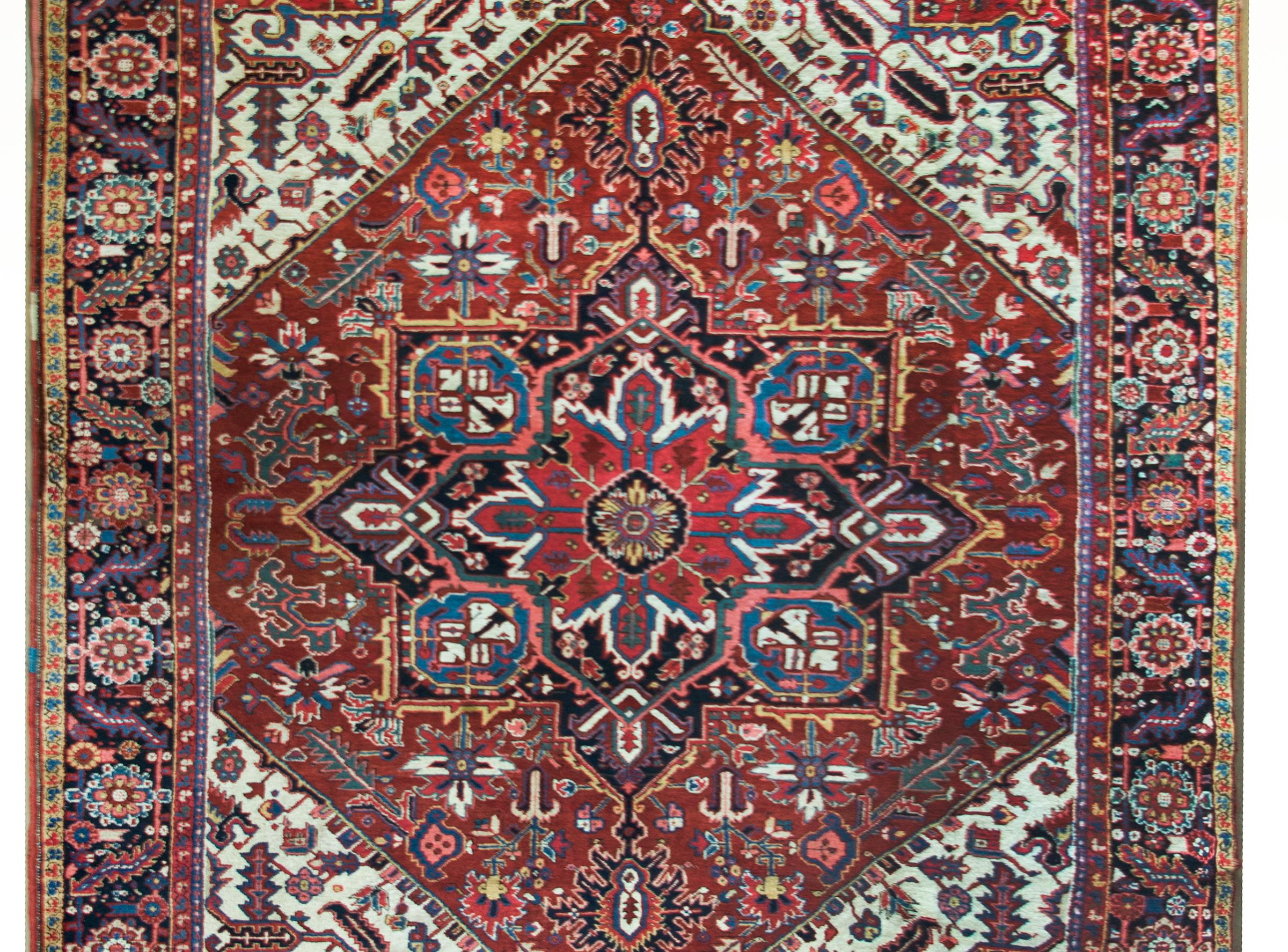 A stunning early 20th century Persian Heriz rug with a large central floral medallion amidst a field of more flowers and scrolling vines, surrounded by a complex border with a large-scale repeated floral pattern flanked by mismatched pairs of petite