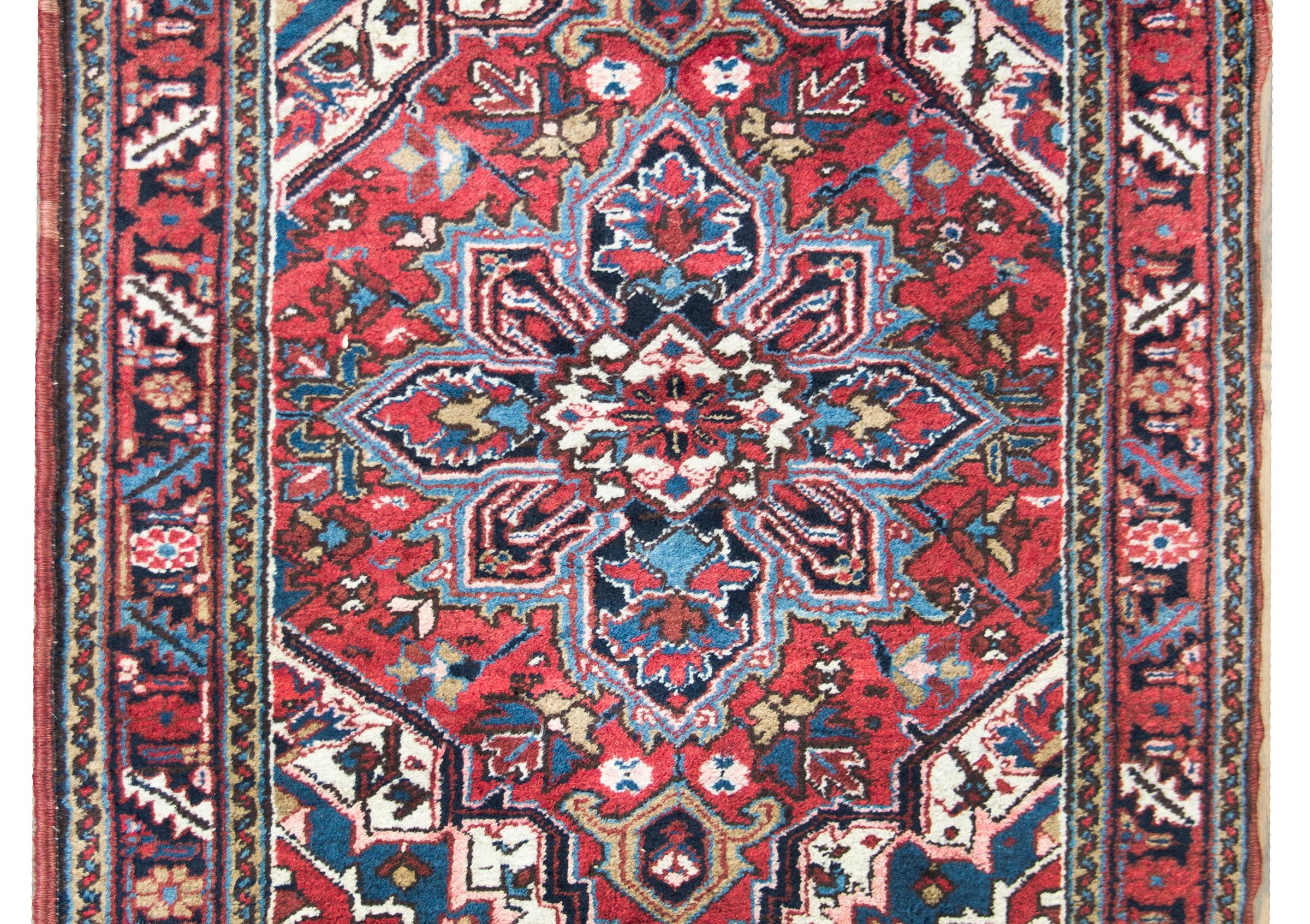 A beautiful early 20th century Persian Heriz rug with a traditional large central floral medallion living amidst a field of more flowers and leaves, surrounded by a repeated leaf and floral pattern, and all woven in crimson, light and dark indigo,