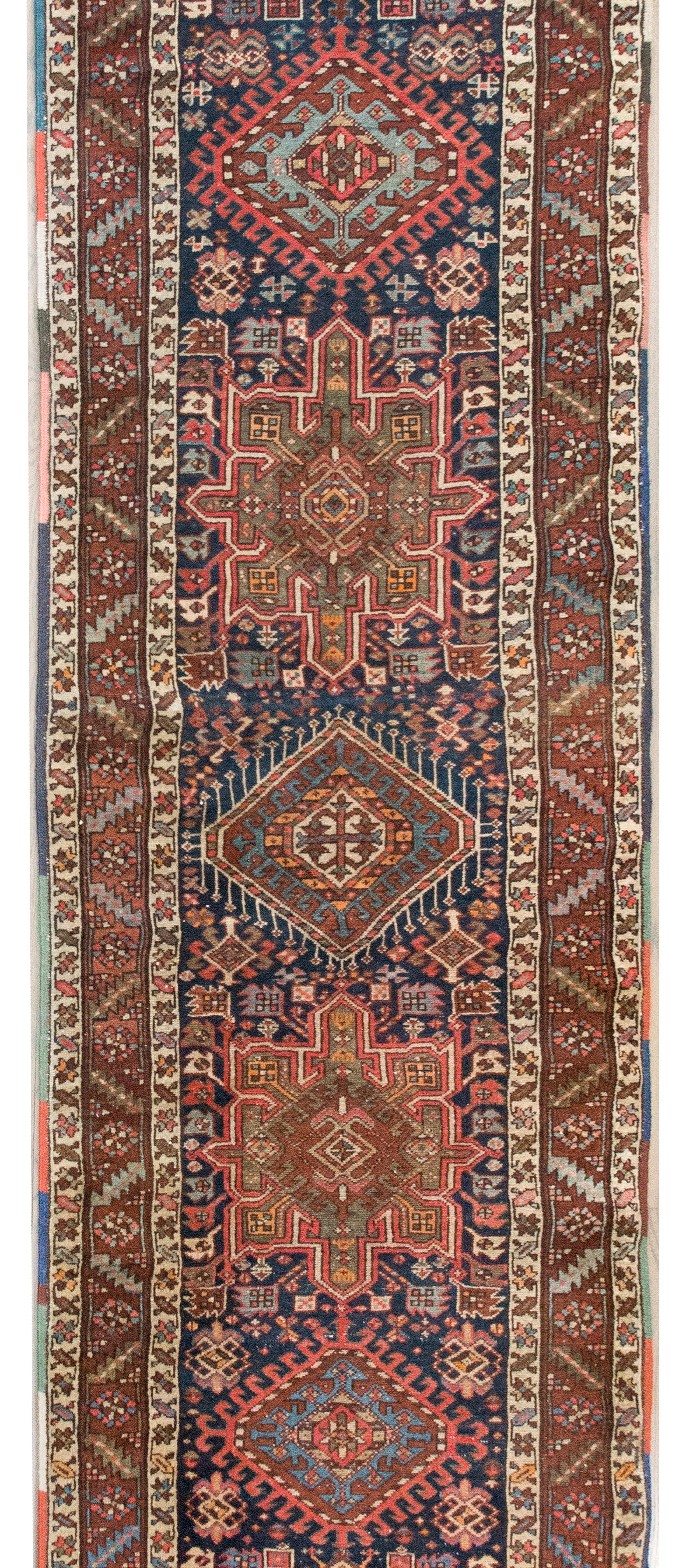A gorgeous early 20th century Persian Heriz runner with multiple stylized floral medallions living in a densely woven field of stylized flowers, and surrounded by petite and large scale floral striped borders, and all woven in varying shades of