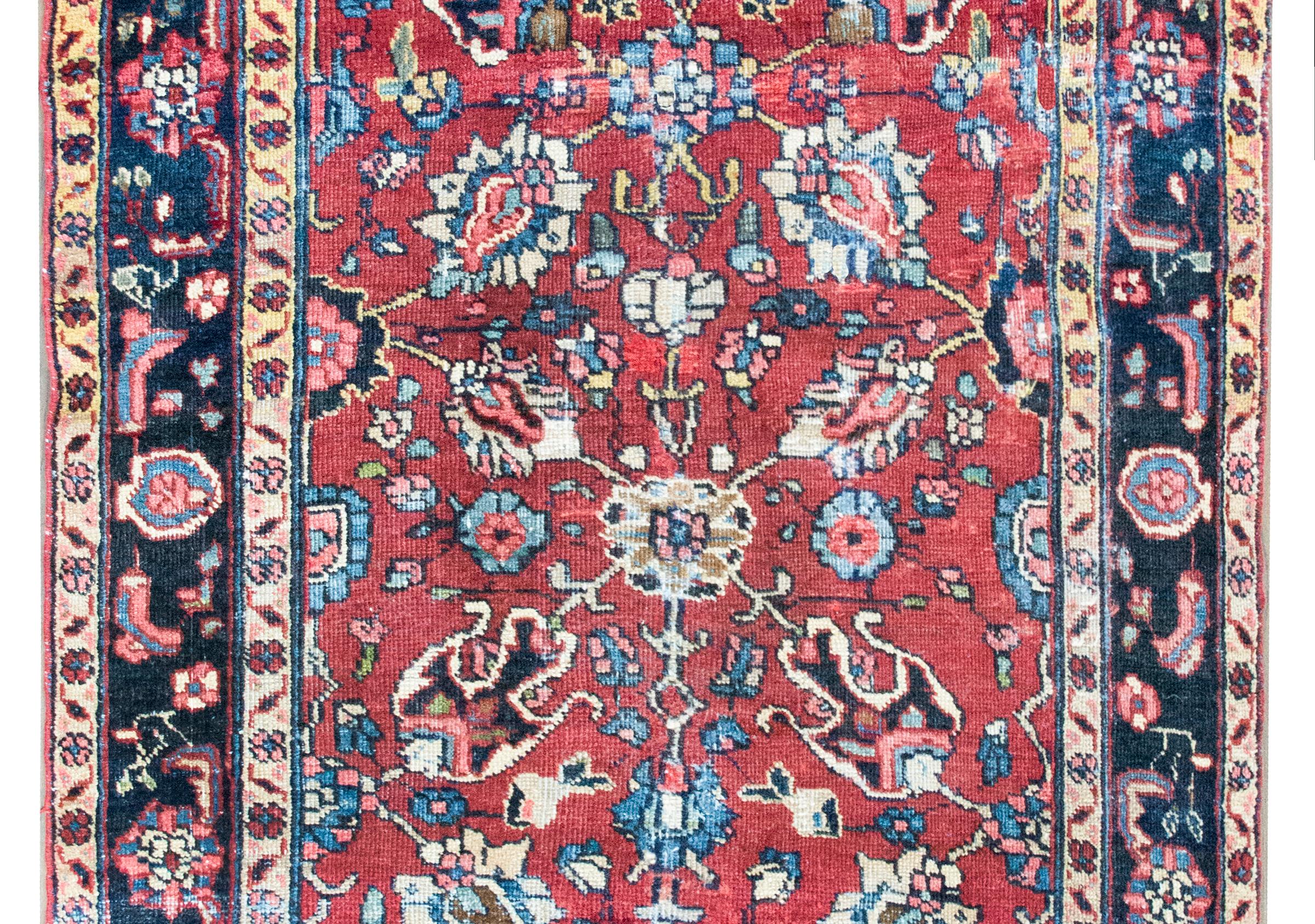 A hand knotted early 20th century Persian Heriz rug with a large-scale floral and leaf patterned field surrounded by a wide border with a repeated pattern of stylized flowers, and all woven in crimson, light and dark indigo, pink, and cream colored