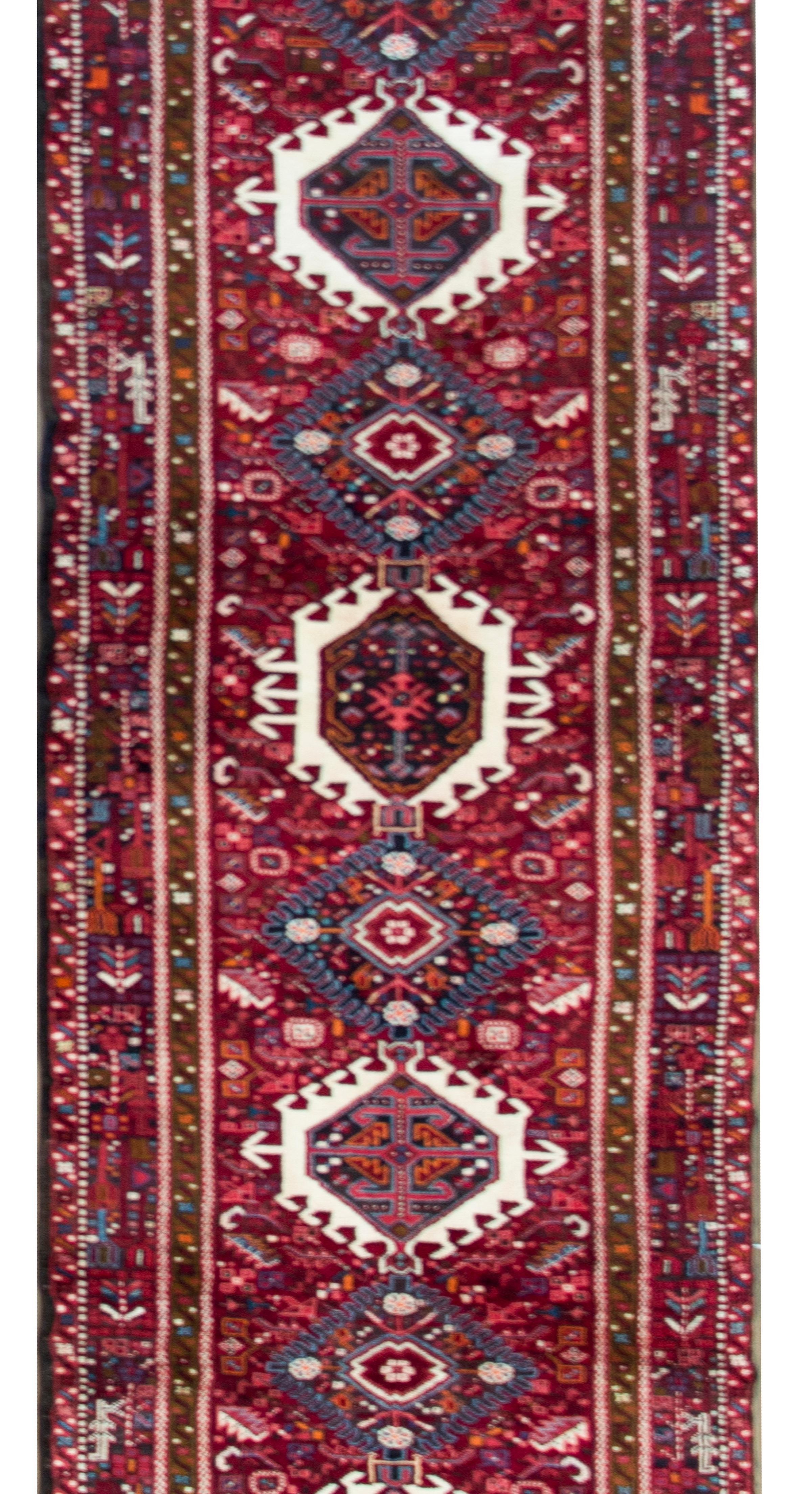 A beautiful MId-20th century Persian Heriz runner with several large stylized floral medallions living amidst a densely woven field of flowers, and surrounded by a complex floral and paisley border woven in myriad colors including crimson, gold,