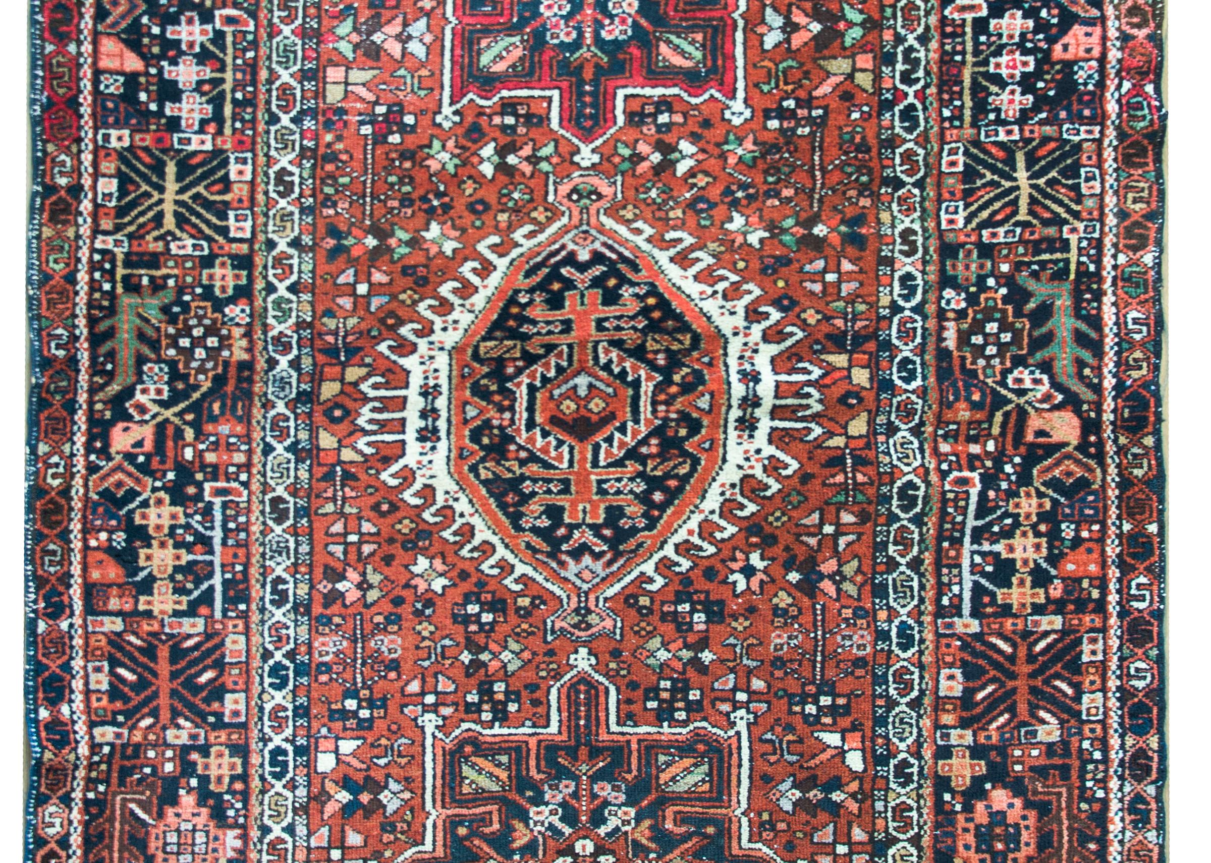 A striking early 20th century Persian Karaja rug with a tribal pattern containing three large central medallions heavily woven with stylized flowers, and living amidst a field of even more stylized flowers, surrounded by a wide border with a