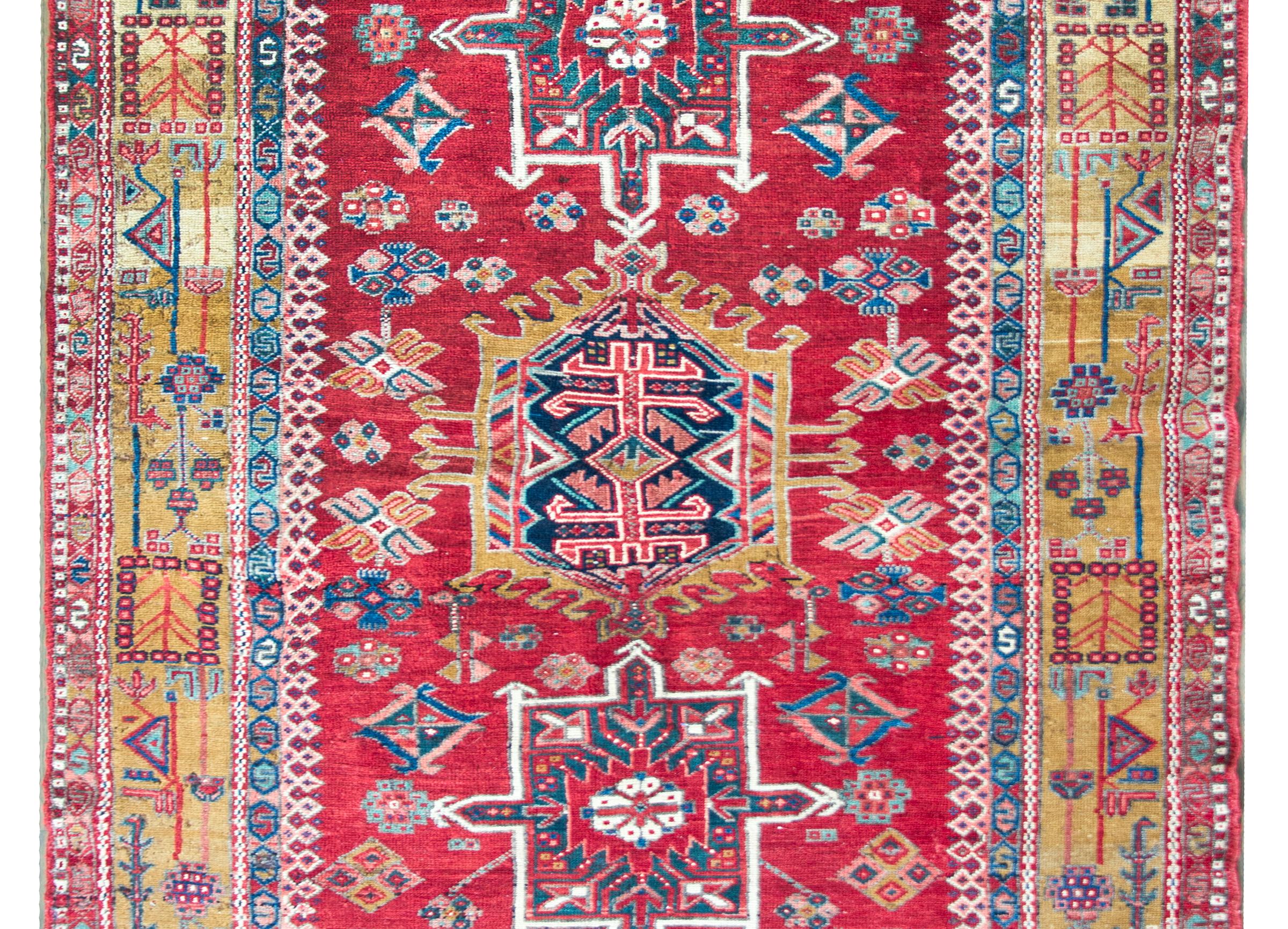 A striking early 20th century Persian Karaja rug with a tribal pattern containing three large central medallions heavily woven with stylized flowers, and living amidst a field of even more stylized flowers, surrounded by a wide border with a