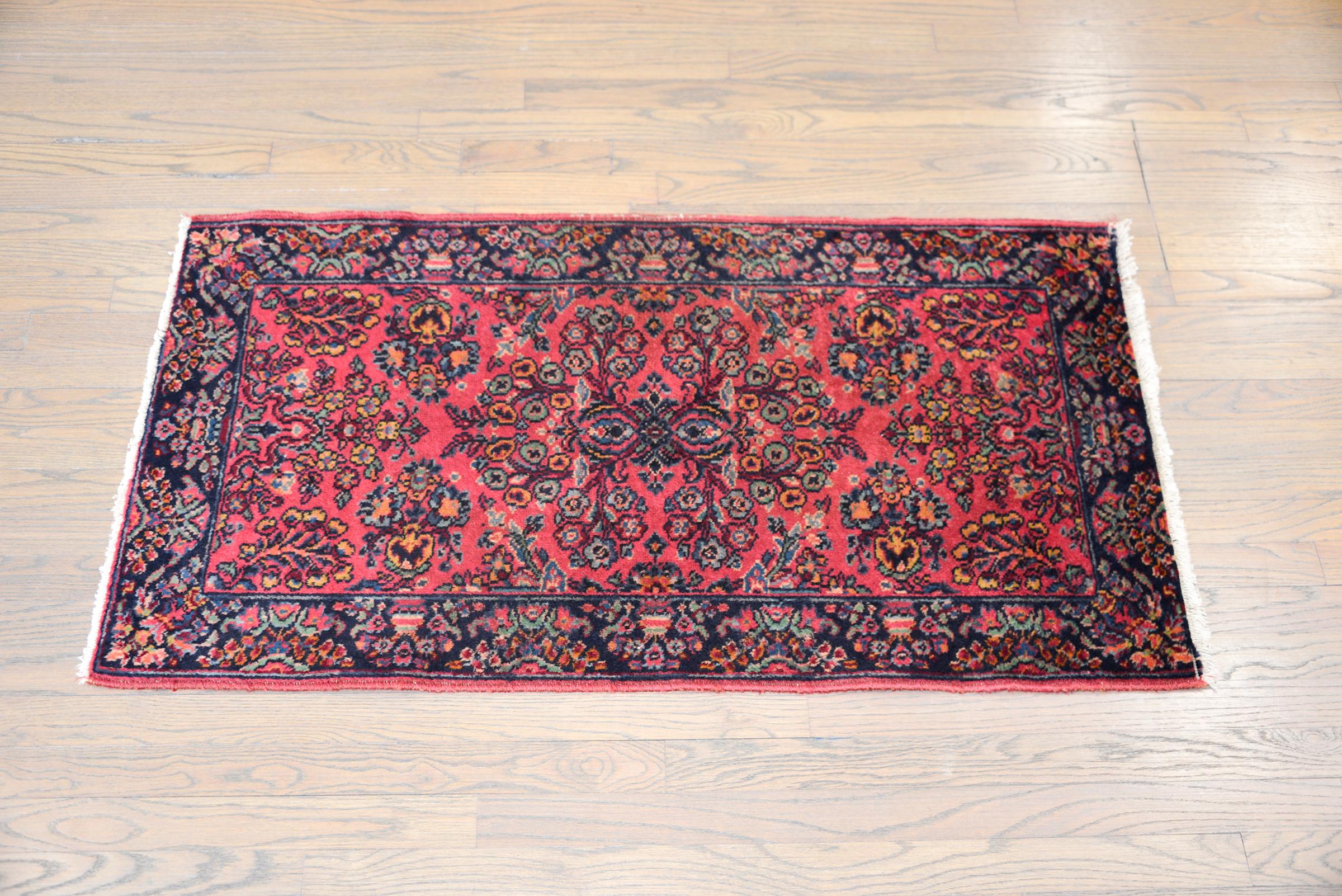 An early 20th century Persian Karastan Sarouk patterned rug with an all-over floral and leaf pattern woven in light and dark indigo, gold, teal, and all set against a pink background. The border is sweet with a floral and tree-of-life pattern woven