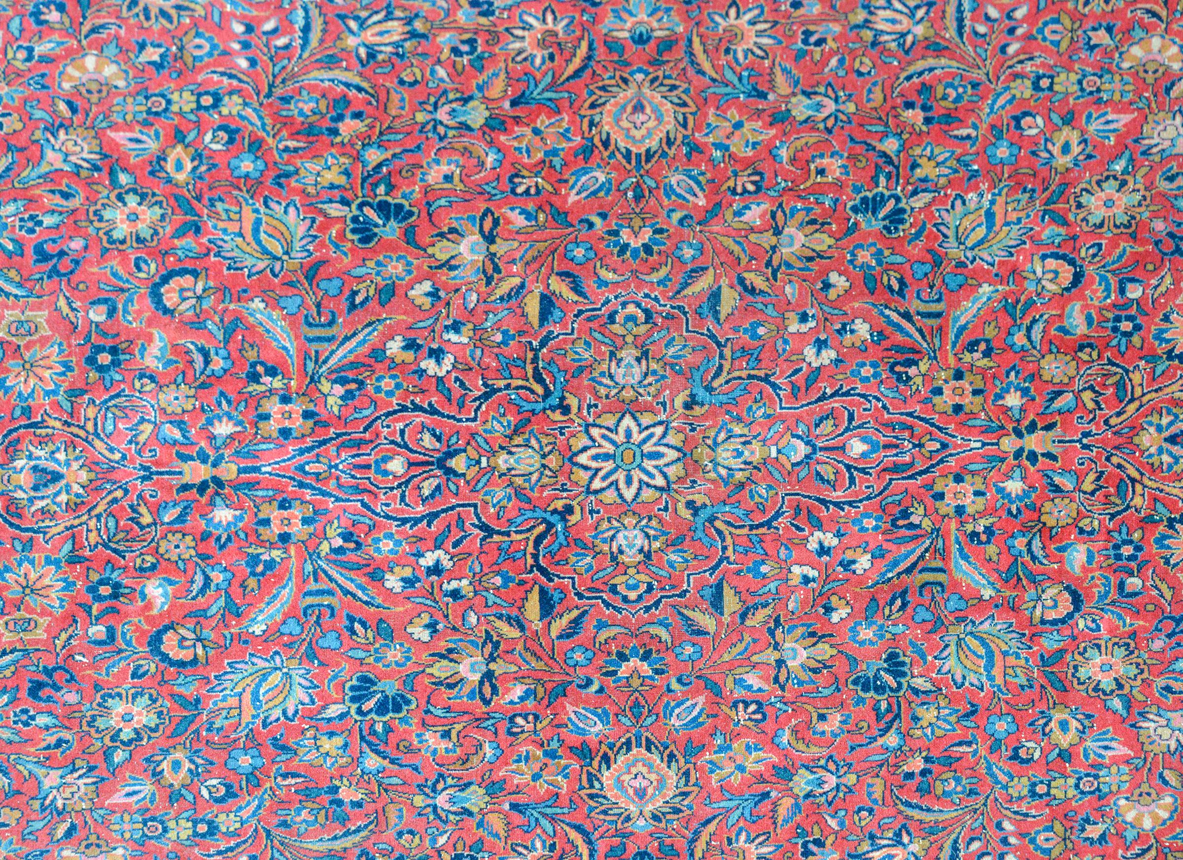 Un fantastico tappeto persiano Kashan dell'inizio del XX secolo con un motivo floreale e fogliare specchiato all-over tessuto in una miriade di colori, tra cui indaco chiaro e scuro, oro, rosa e crema, su uno sfondo color mirtillo rosso, e