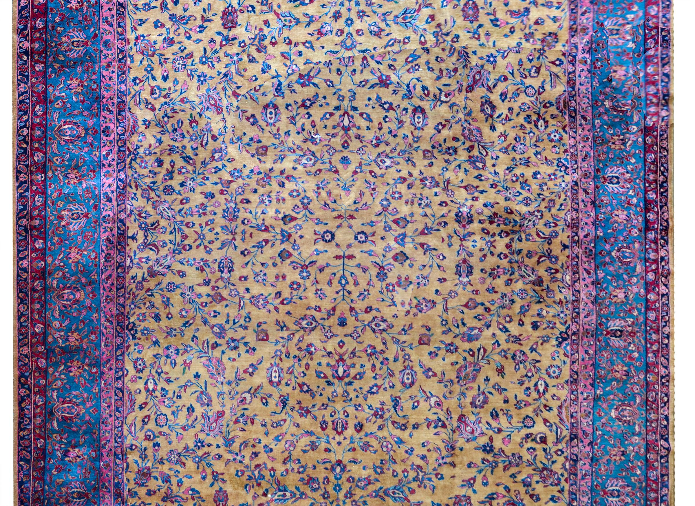 An incredible early 20th century Persian Kashan rug with a beautiful yellow field with a mirrored floral and scrolling pattern woven in pinks, indigos, and greens, and surrounded but a wide complex border containing a wide central floral patterned
