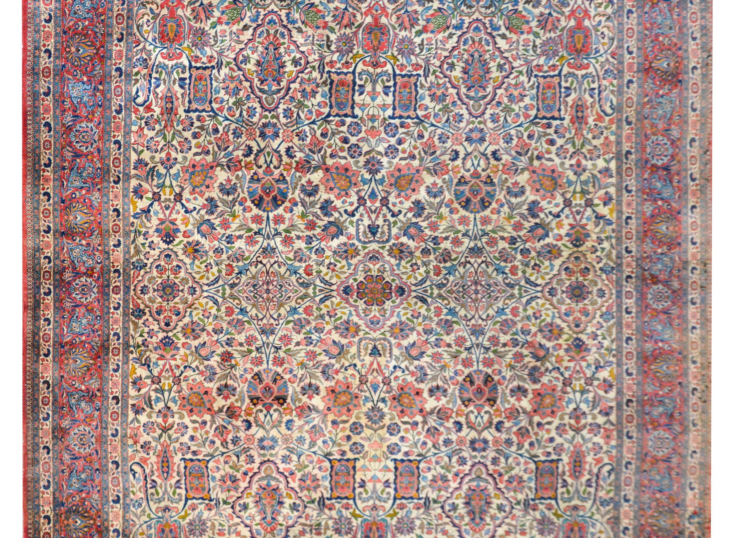 A wonderful early 20th century Persian Kashan rug with an all-over trellis floral and vine pattern woven in myriad colors including crimson, indigos, greens, golds, and pinks, set against a cream colored background, and surrounded by an incredible