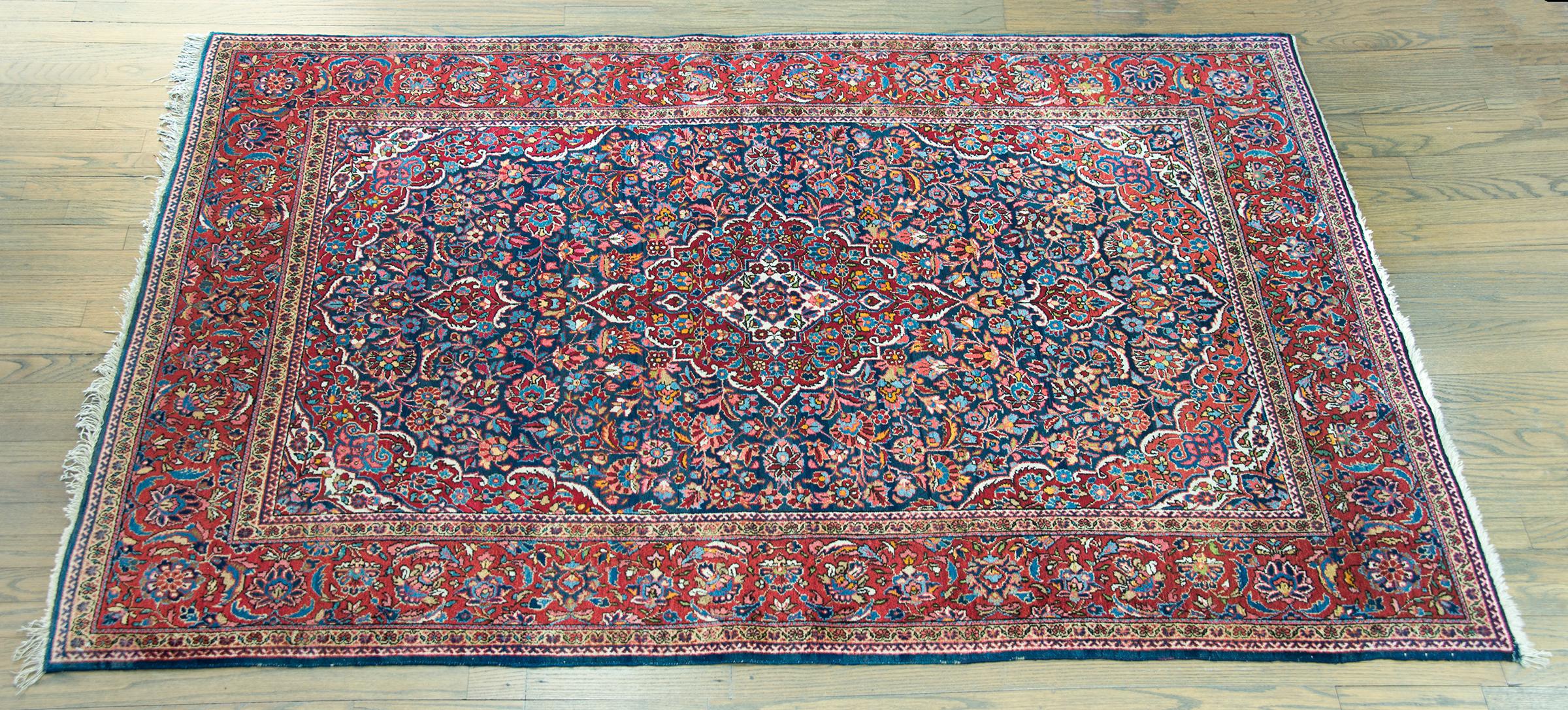 A striking early 20th century Persian Kashan rug with a central medallion living amidst a field of tightly woven flowers and leaves, surrounded by a wide floral border flanked by pairs of petite flowers, and all woven in brilliant crimsons, indigos,