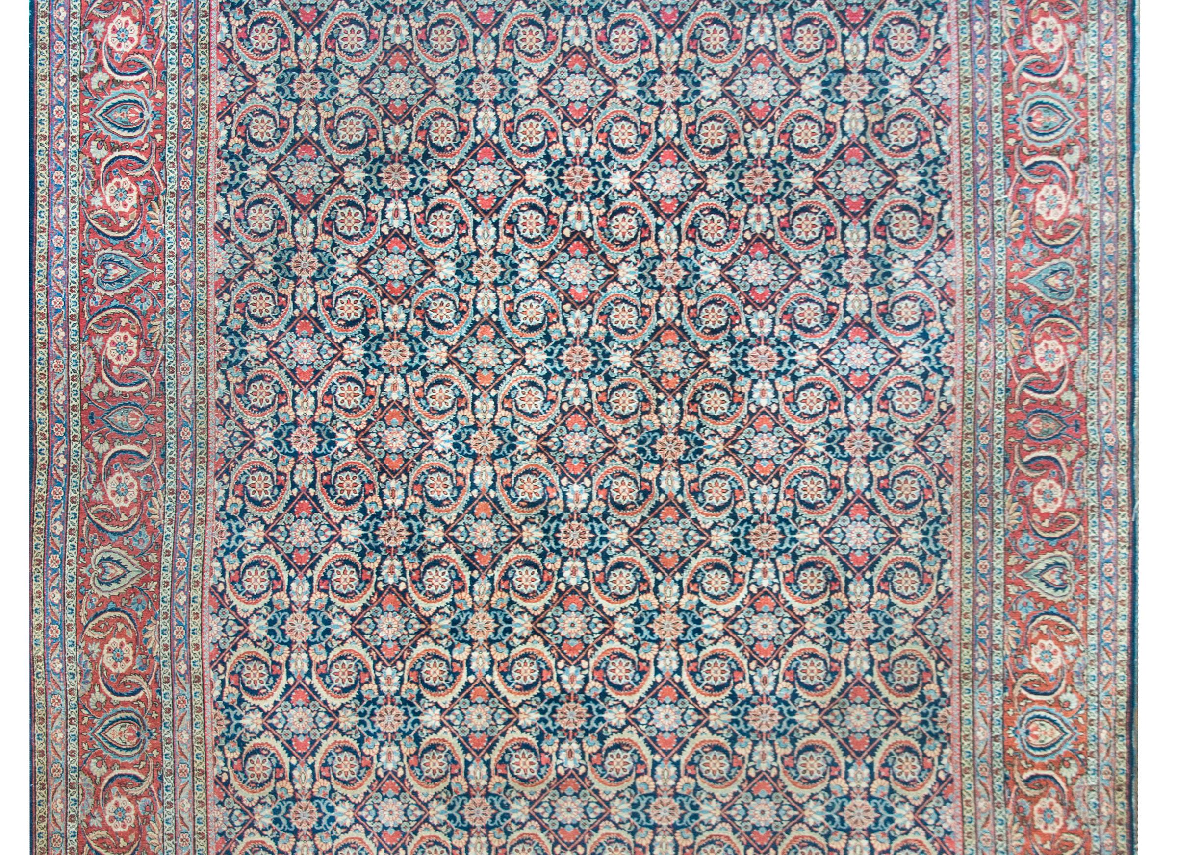 A fantastic early 20th century Persian Kashan rug with an all-over trellis floral pattern with myriad flowers, leaves, and vines, and all woven in crimson, cream, light and dark indigo, and surrounded by a wide floral partnered border with a central