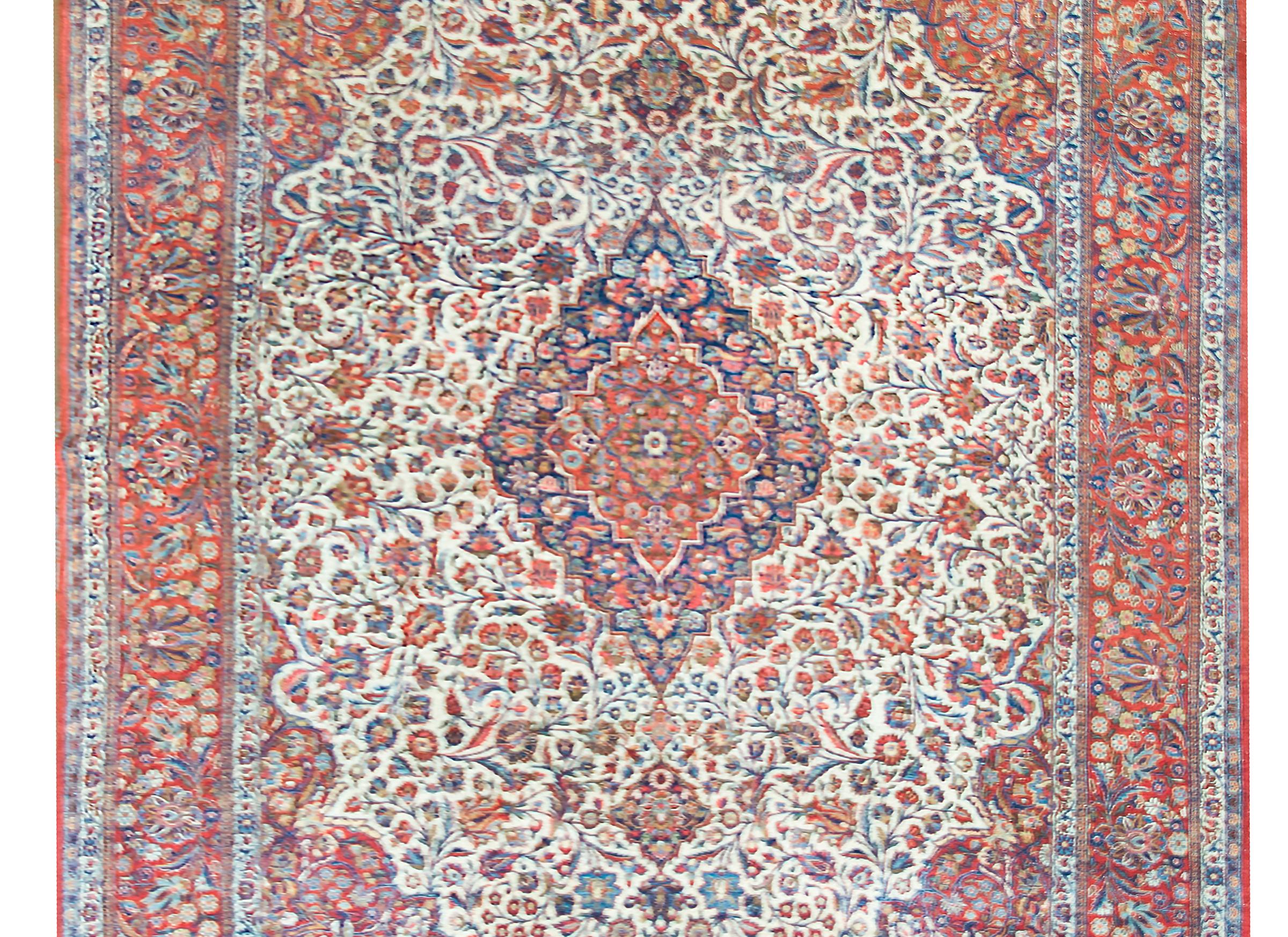 A wonderful early 20th century Persian Kashan rug with a large central floral medallion living amidst a field of even more densely woven flowers and vines, woven in myriad colors including crimson, gold, light and dark indigo, and pink, and