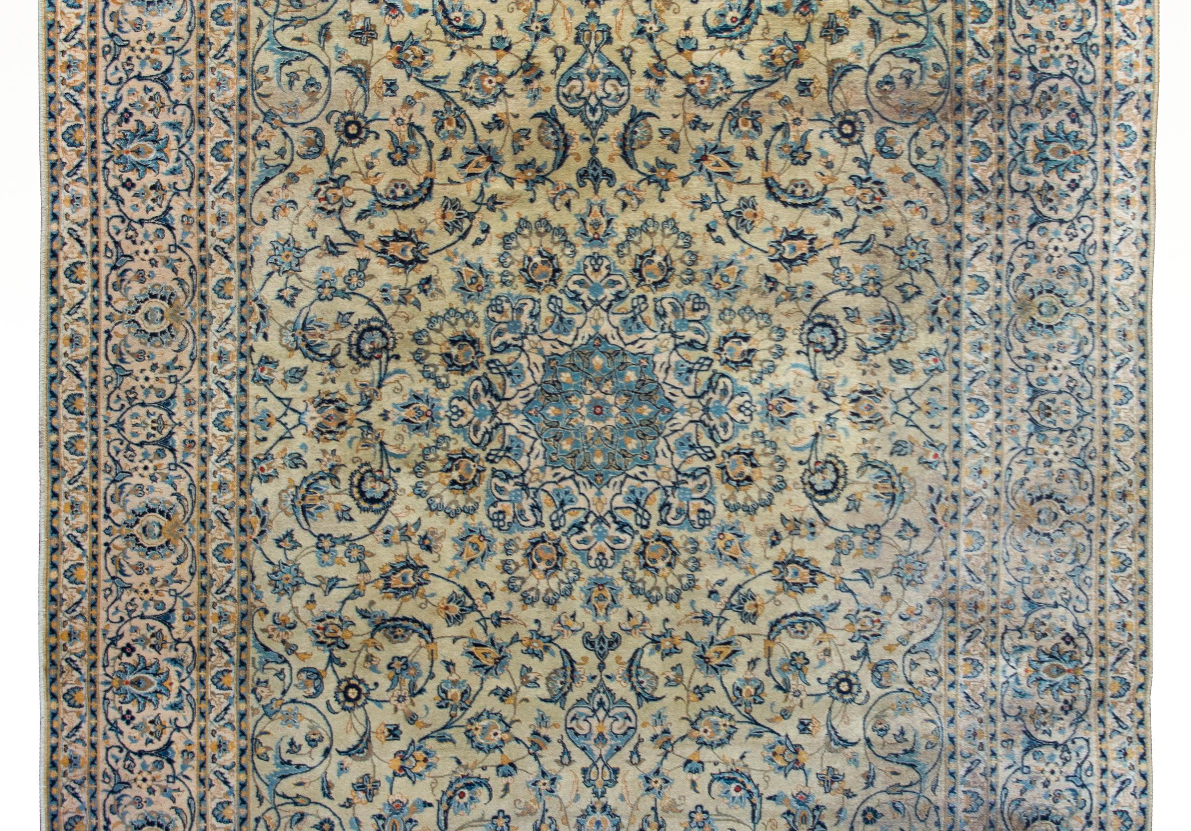 Magnifique tapis persan du début du XXe siècle de Kashan, avec un grand médaillon central flottant orné d'une myriade de fleurs et de vignes enroulées, rendu de manière experte, et tissé dans des tons variés d'indigo, de crème, d'or et de brun, le