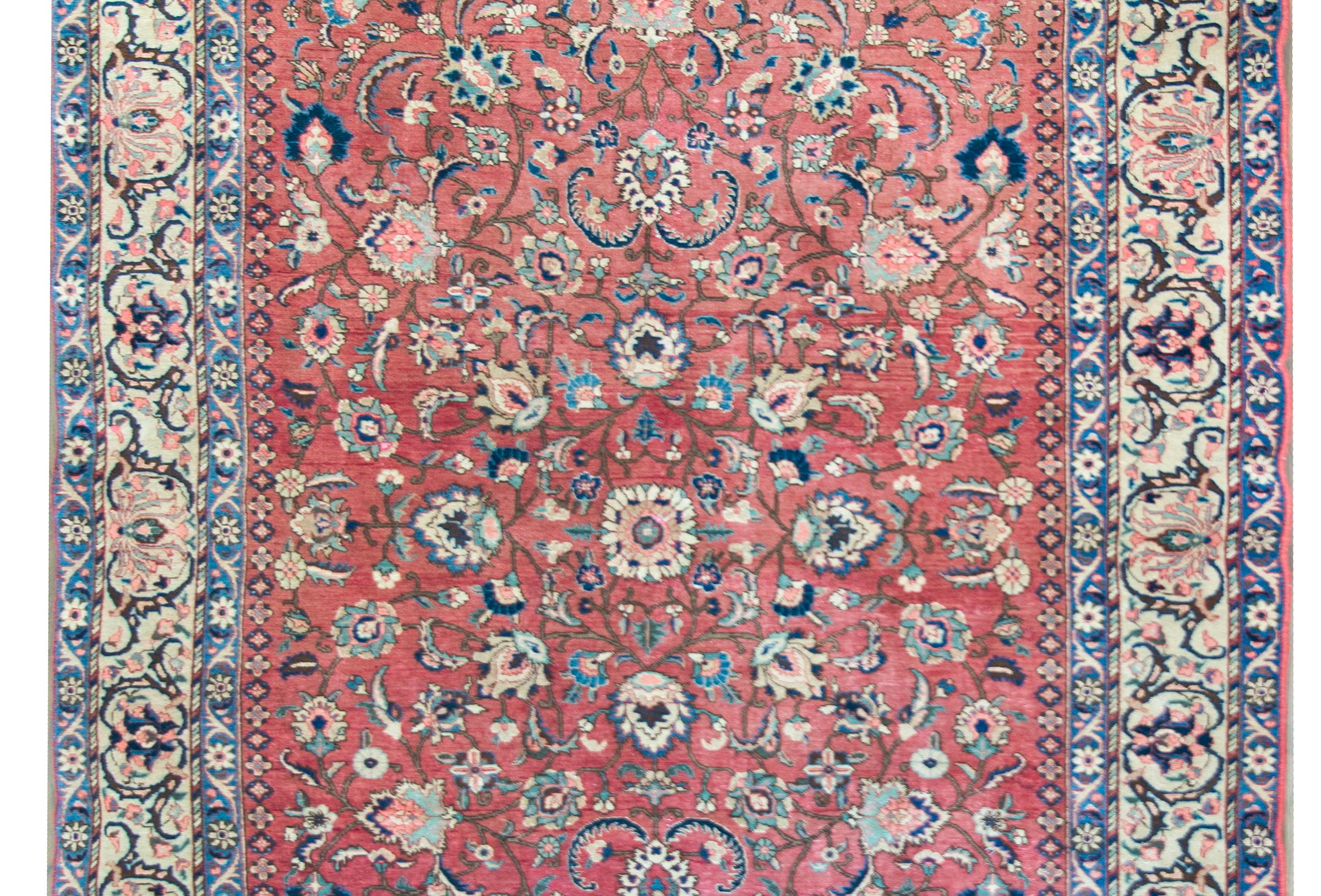 A gorgeous early 20th century Persian Khoy rug with an elaborate all-over mirrored floral pattern with a central flower surrounded by intricate scrolling vines and more flowers, surrounded by a complex border with a wide central floral stripe