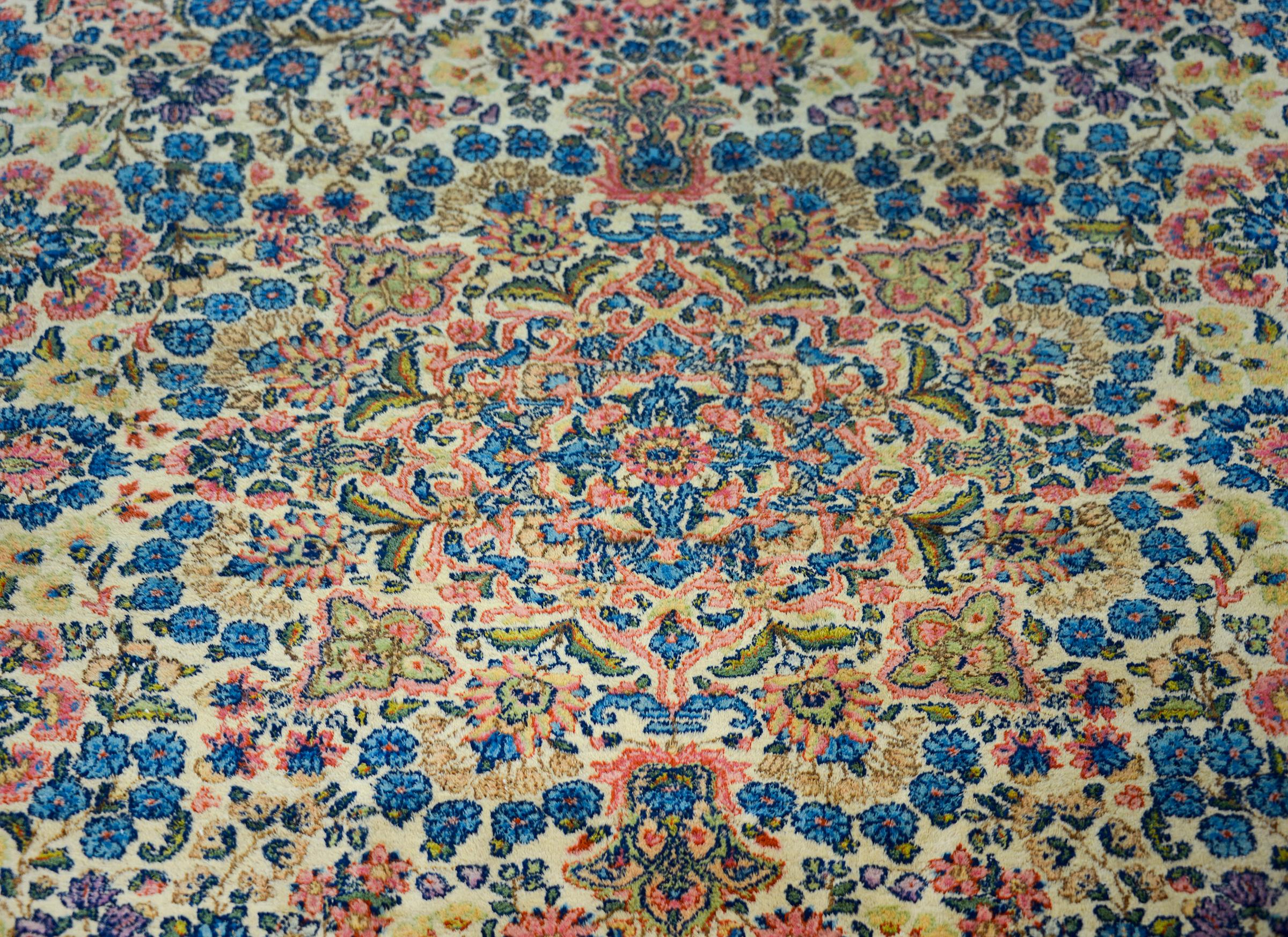 A wonderful early 20th century Persian Kirman rug with an incredible all-over mirrored floral cluster pattern containing myriad flowers and woven in myriad colors including traditional Kirman pinks, indigos, creams, and greens. The border is
