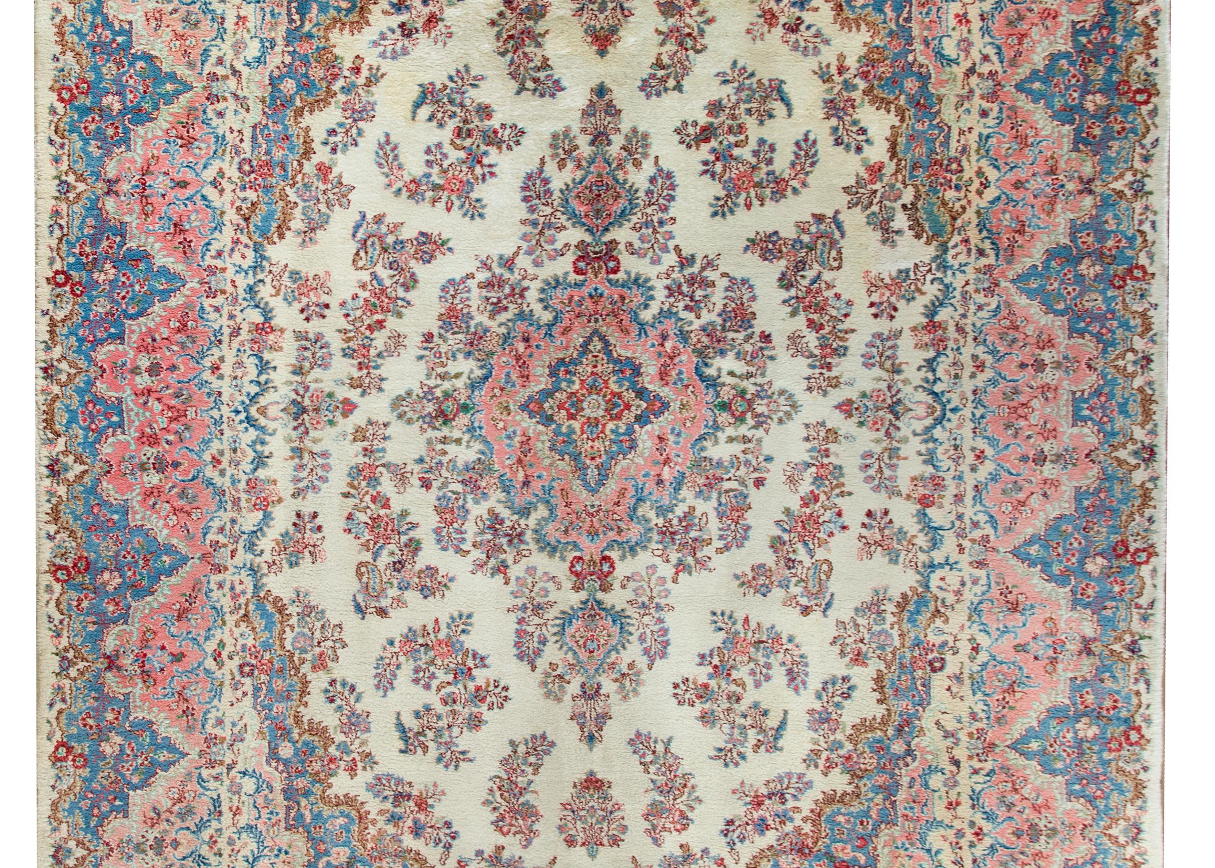 A stunning early 20th century Persian Kirman rug with a mesmerizing floral pattern radiating out from the center, and woven in pinks, indigos, crimsons, and whites. The border is extraordinarily wide with a wonderful floral pattern similar to the