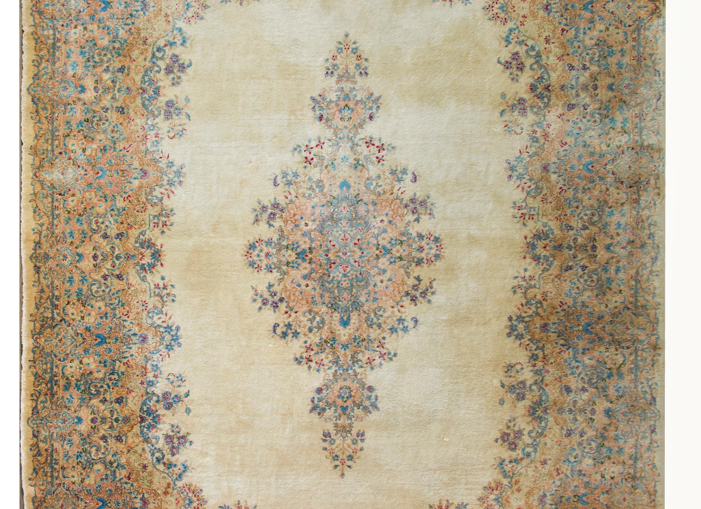 A beautiful early 20th century Persian Kirman rug with a large central floral medallion woven in crimson, peach, green, and light and dark indigo, and set against a cream colored background.  The border is exceptional and wide, and woven with a