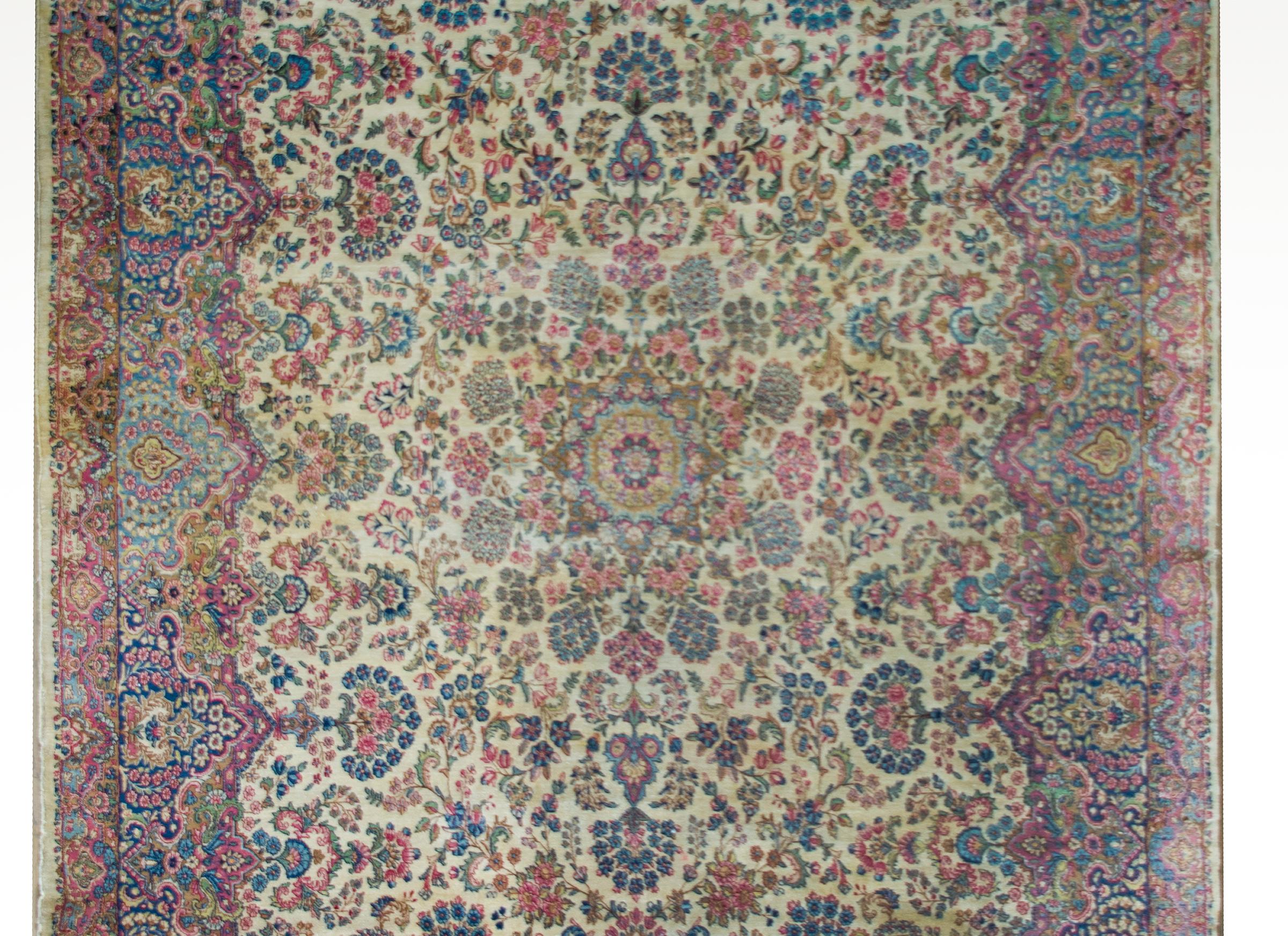 A mesmerizing early 20th century Persian Kirman rug with an all-over kaleidoscope of a pattern containing myriad floral clusters woven in traditional Kirman colors including pink, crimson, green, and light and dark indigo, and set against a cream