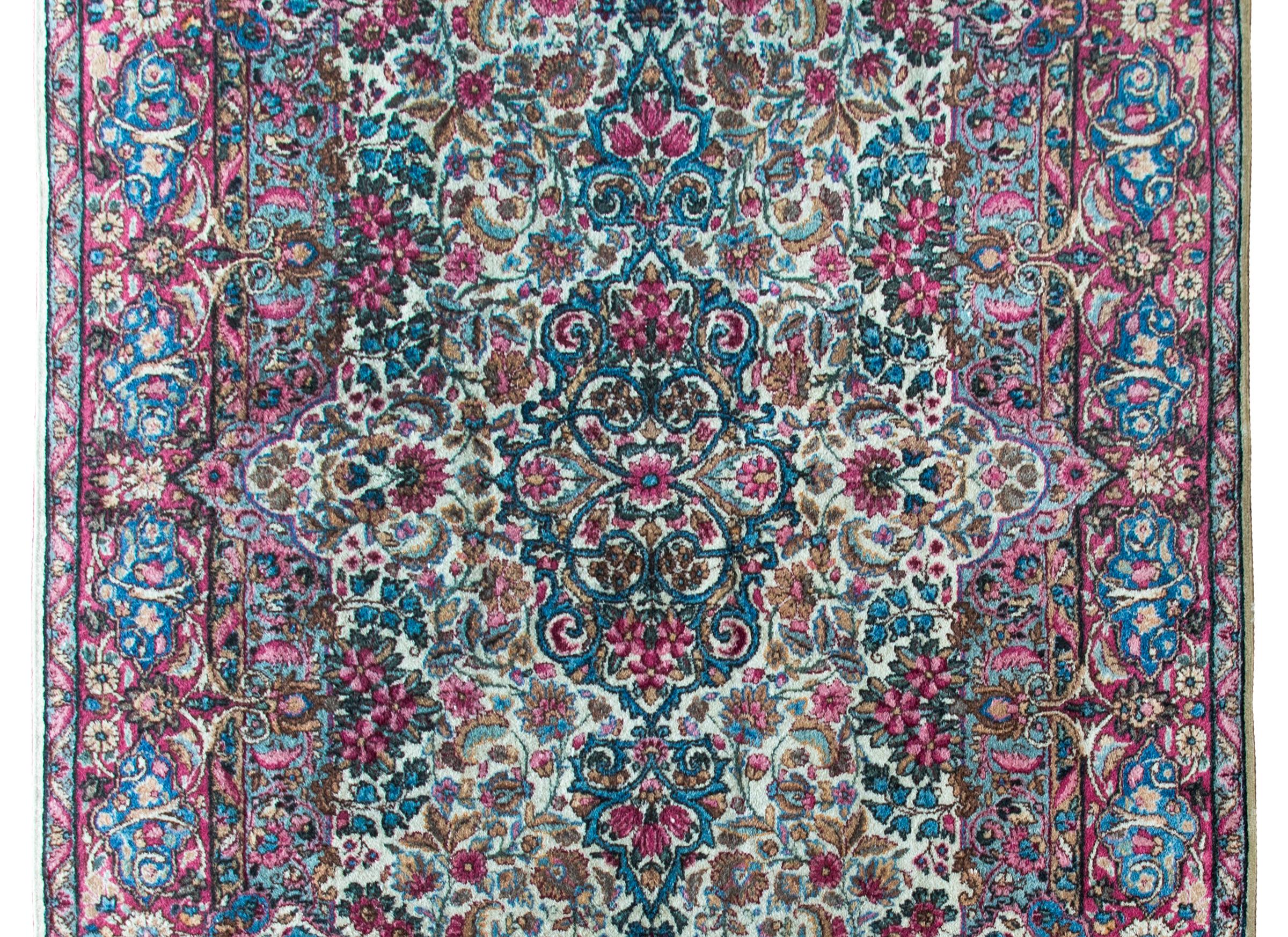 A beautiful early 20th century Persian Kirman rug with an all-over mirrored densely woven floral pattern with myriad flowers, surrounded by an incredible floral patterned border and all woven in traditional Kirman colors of cream, light and dark
