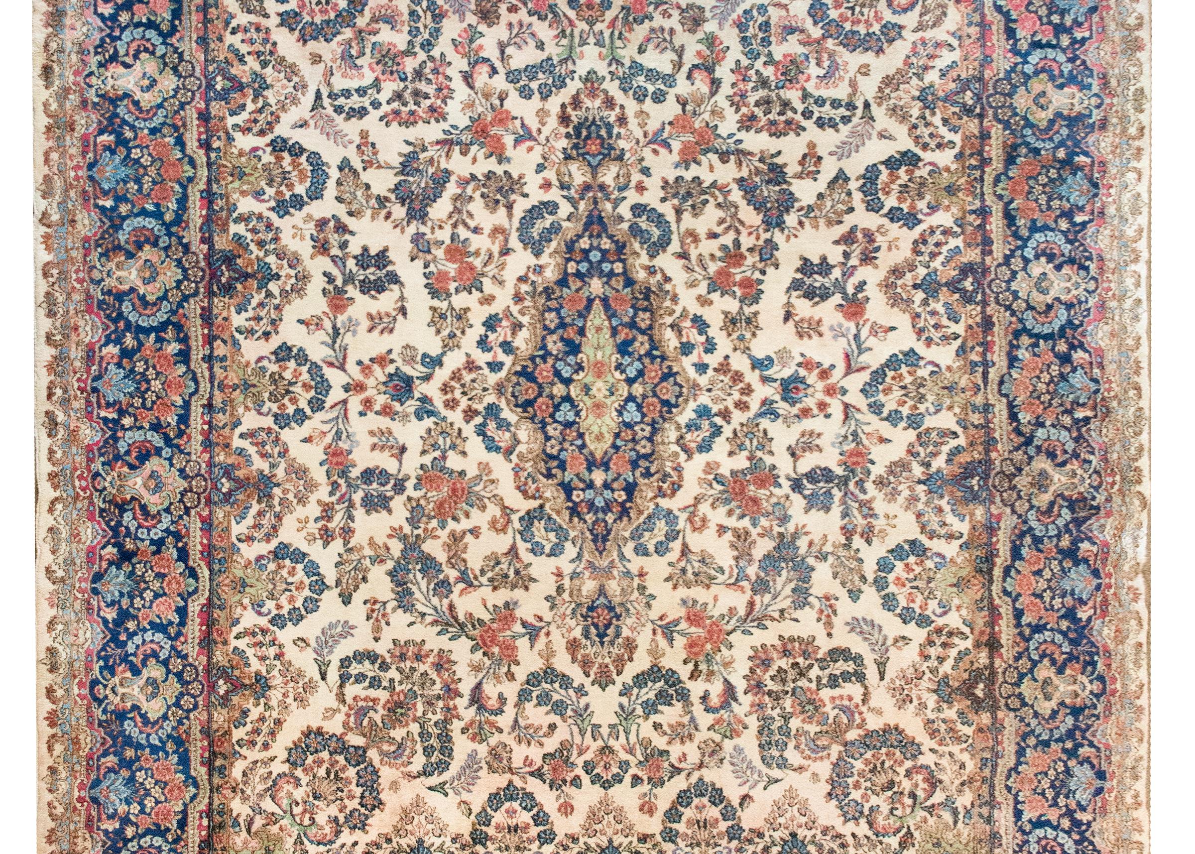 Un bellissimo tappeto persiano Kirman dell'inizio del XX secolo con un grande medaglione floreale centrale che vive in un campo di fiori ancora più raggruppati, circondato da un'ampia ed elaborata bordura con fiori ripetuti e rampicanti, il tutto