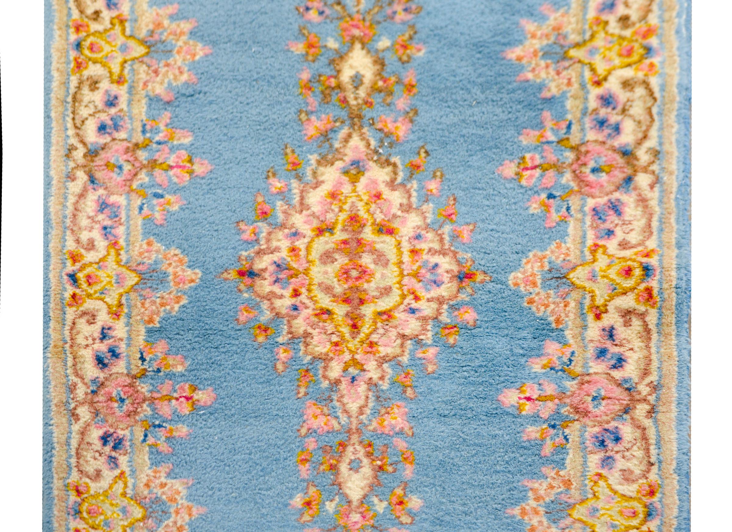A sweet early 20th century Persian Kirman runner with a delicately rendered floral pattern woven in pinks, yellows, whites, and reds, set against a pale indigo background, and surrounded by a similarly patterned floral border.