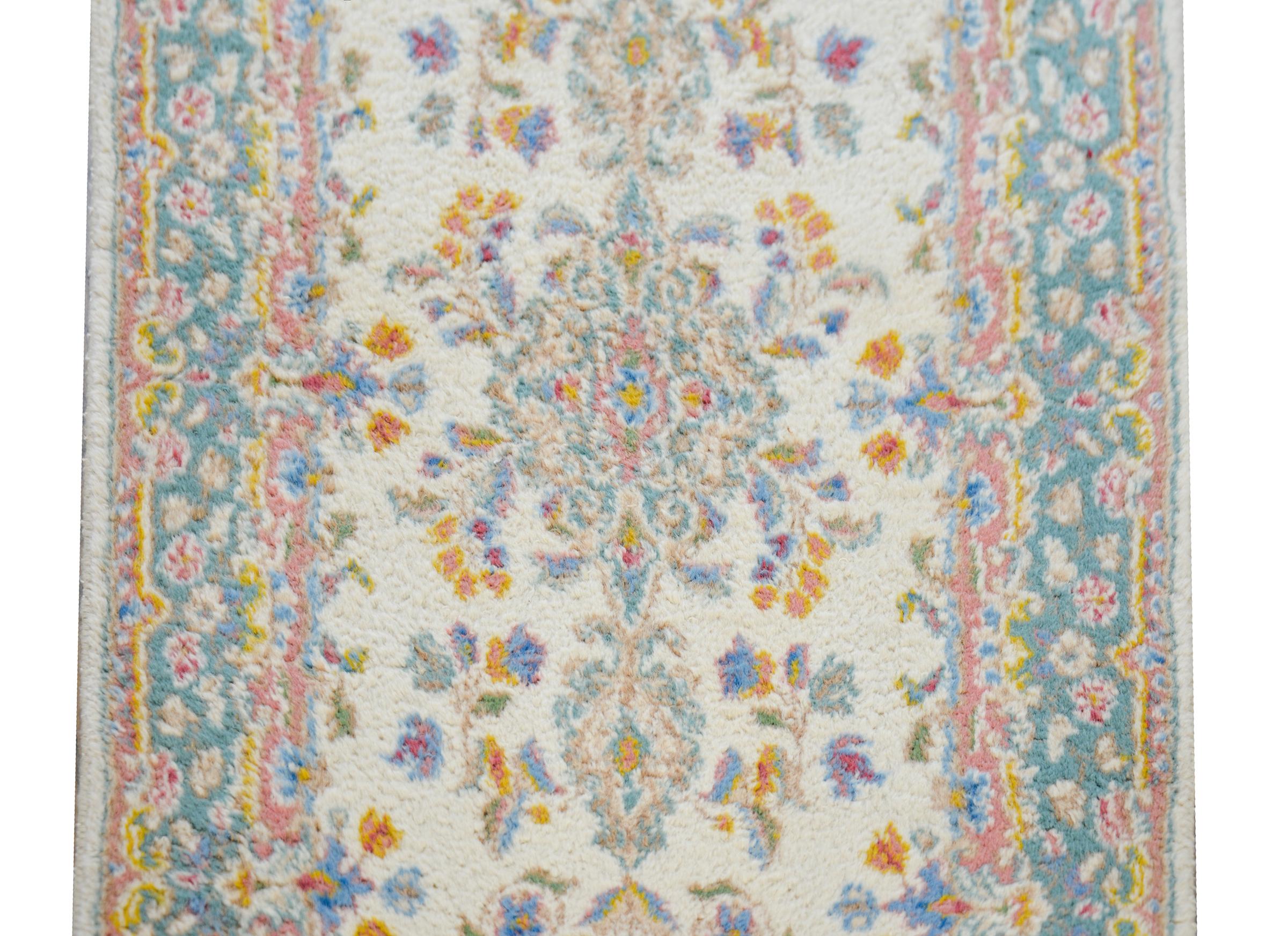 A beautiful early 20th century Persian Kirman runner with a sweet petite floral pattern woven in pinks, golds, oranges, and indigos set against a cream colored ground, and surrounded by a complementary floral patterned border.
