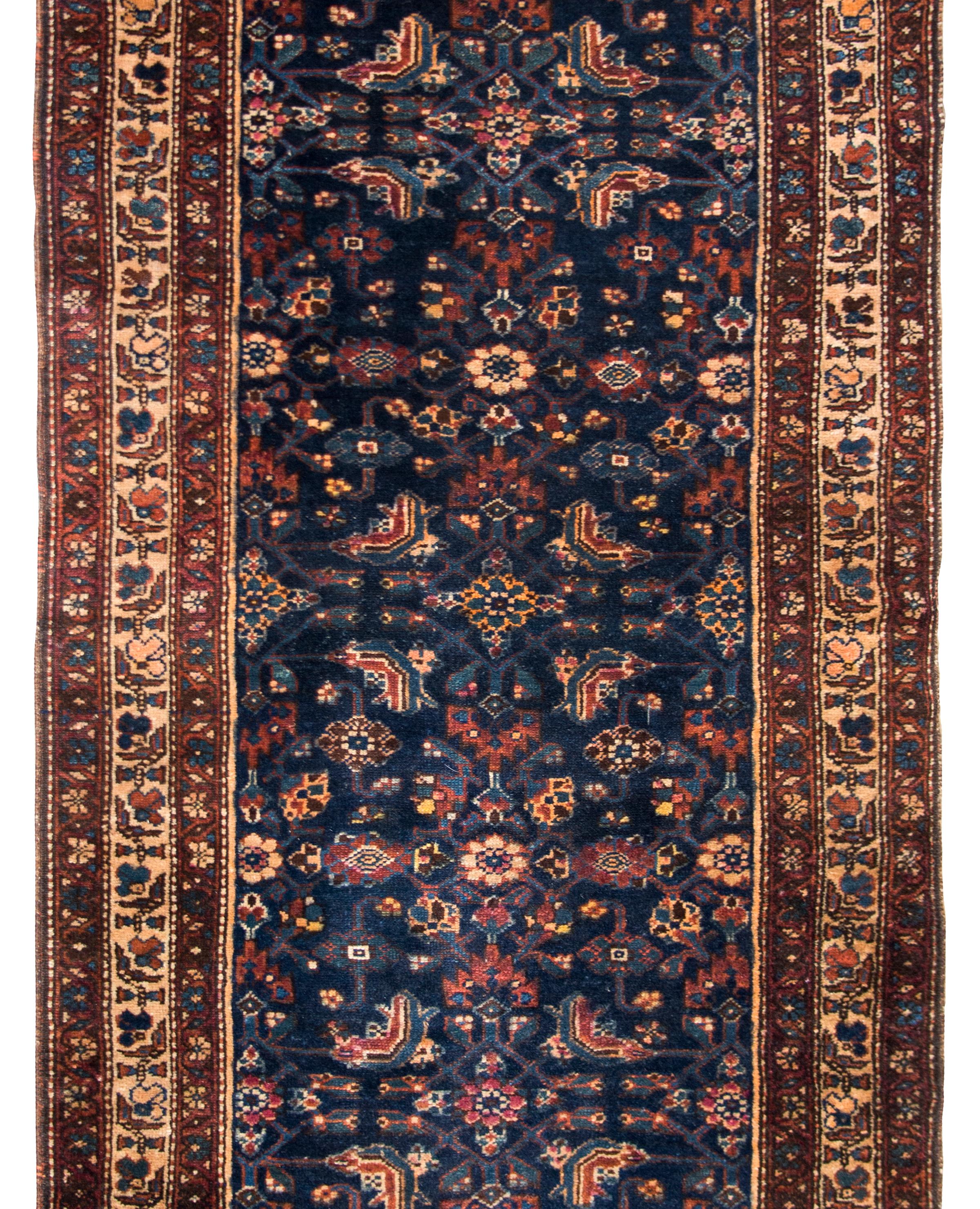 A remarkable early 20th century Persian Kurdish rug with an all-over mirrored trellis floral pattern surrounded by a complex border with several floral patterned and thin geometric patterned stripes, and all woven in dark crimsons, indigos, pinks,