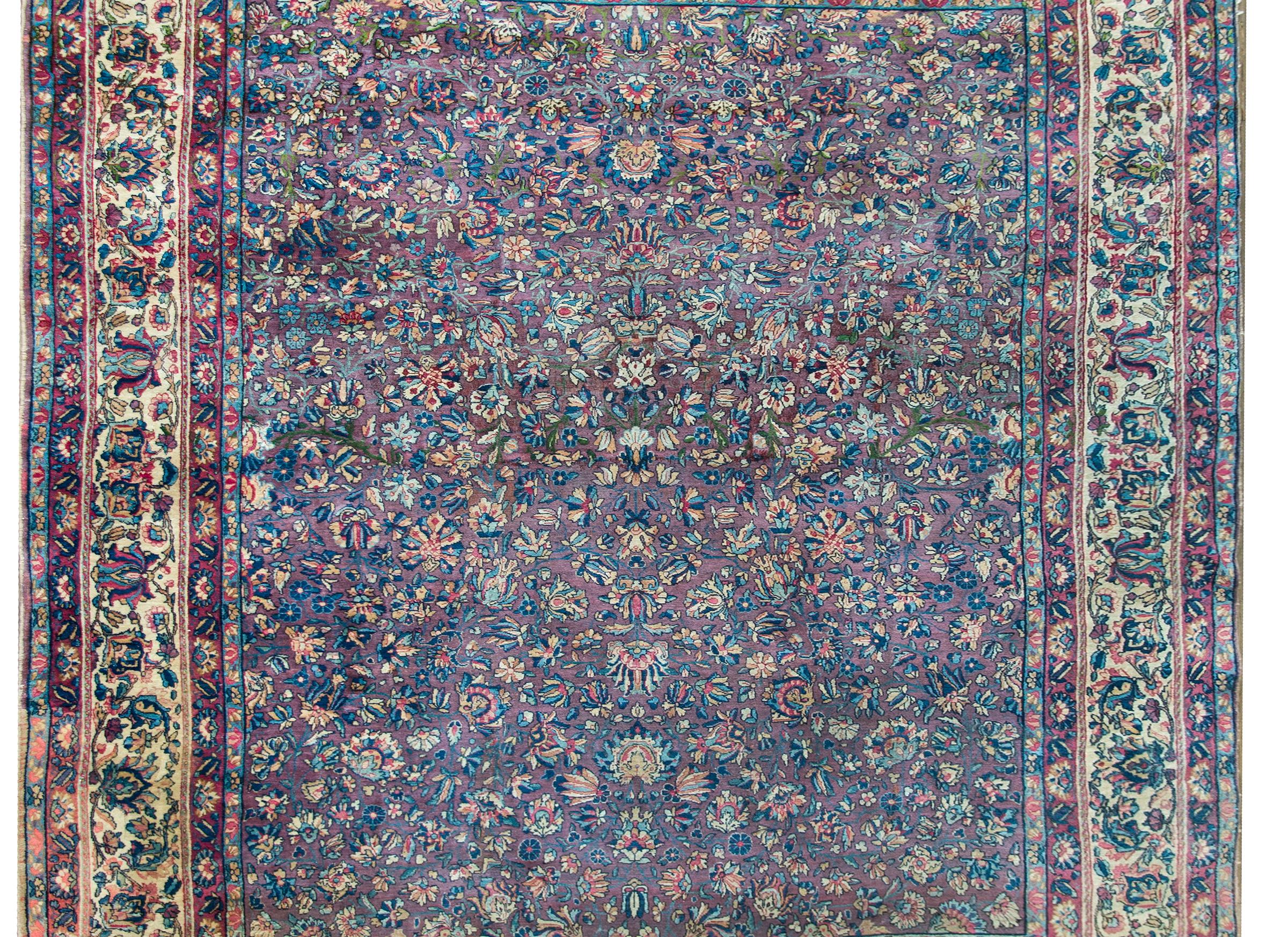 A striking early 20th century Persian Lavar Kirman rug with an all-over mirrored floral pattern with myriad flowers and leaves woven in brilliant light and dark indigo, white, orange, fuchsia, and set against a highly unusual violet background,