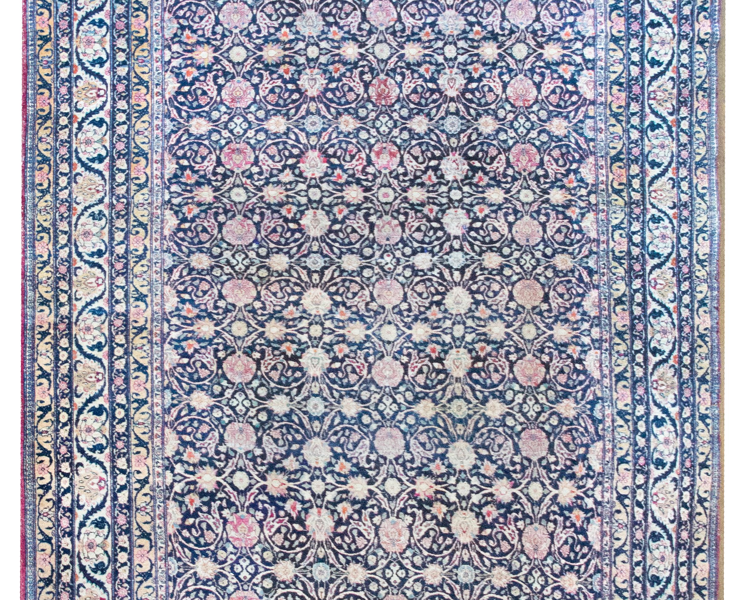 This turn-of-the-20th-century Persian Lavar Kirman rug is a masterful expression of refined elegance and technical virtuosity. Woven with an all-over floral trellis pattern, it features large-scale blossoms and scrolling vines intertwined with a