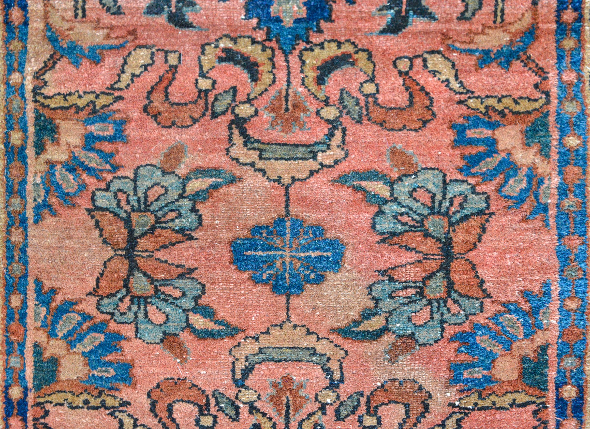 An early 20th century Persian Lilihan rug with a mirrored floral pattern woven in light and dark indigo, cream, and coral, against a pink background, and surrounded by three petite geometric pattered stripes.