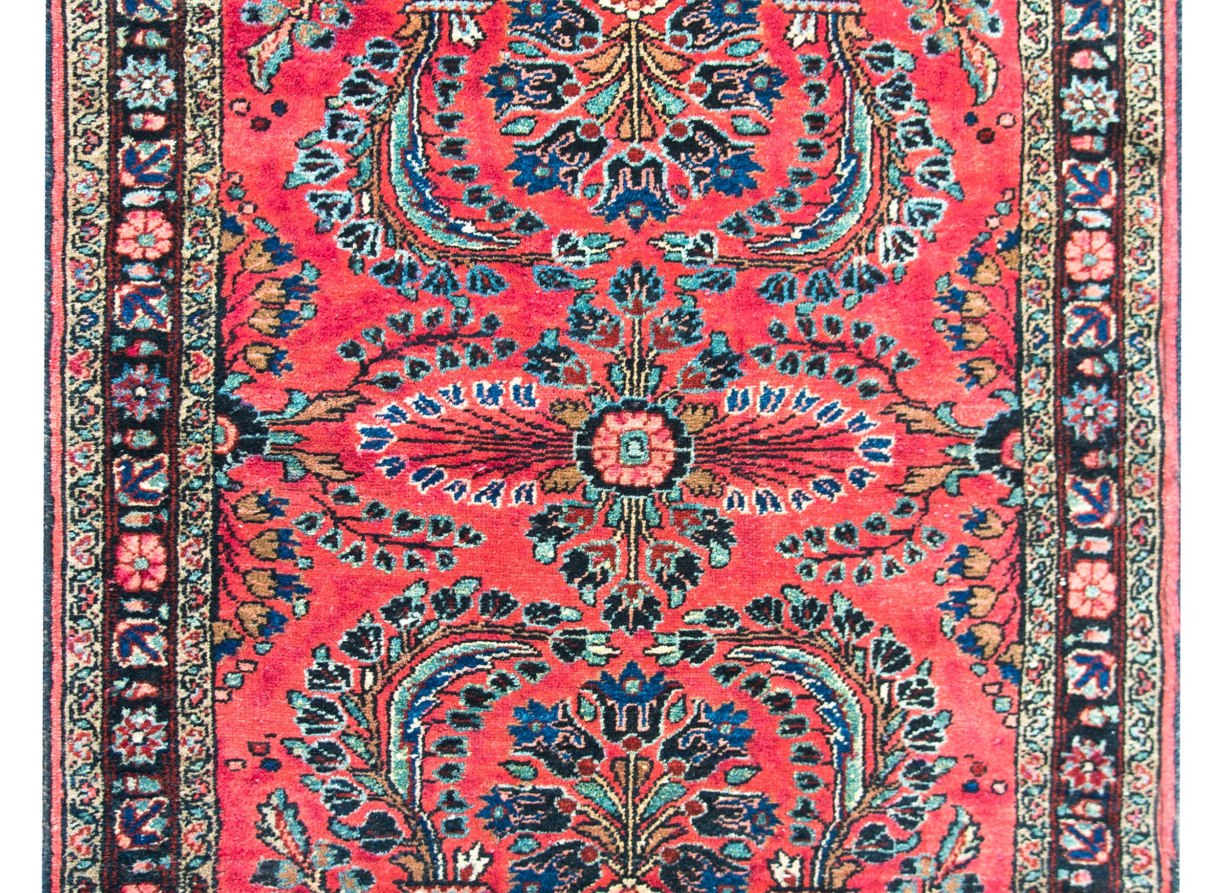 A lovely early 20th century Persian Lilihan rug with a beautiful mirrored floral pattern woven light and dark indigo, pink, brown, white, and black wool, set against a beautiful salmon colored background. The border is sweet, with a central leaf