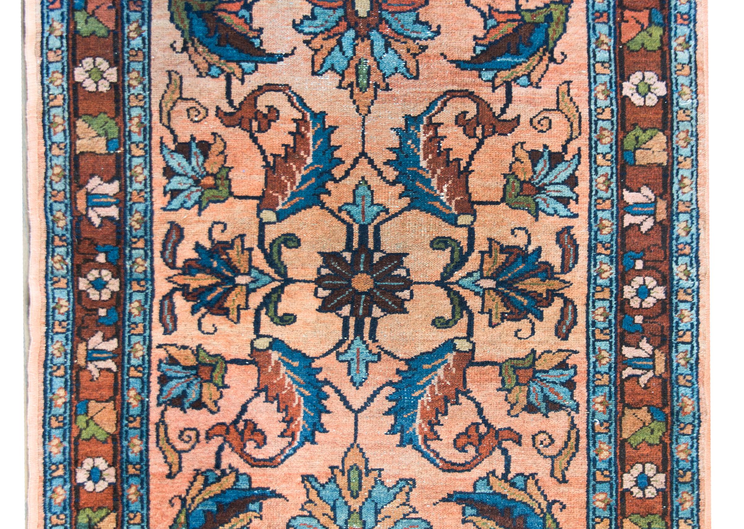 A sweet early 20th century Persian Lilihan rug with a mirrored floral and leaf pattern woven in dark indigo, brick red, brown, and olive green, and set against a salmon colored background. The border is simple with a stylized floral and leaf