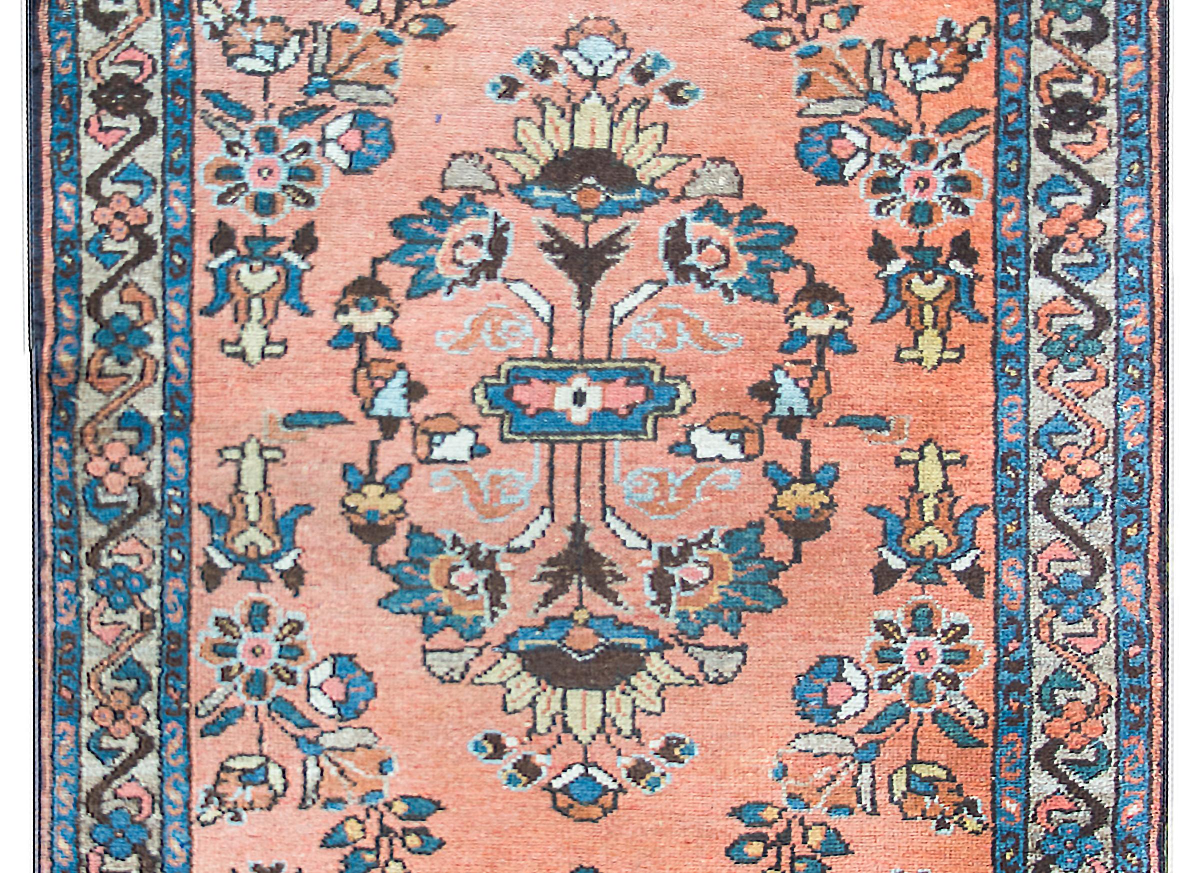 An early 20th century Persian Lilihan rug with a wonderfully rendered mirrored floral pattern woven in indigo, gold, cream, and pink, and set against a coral colored background, and surrounded by a border with stylized flowers and scrolling vines