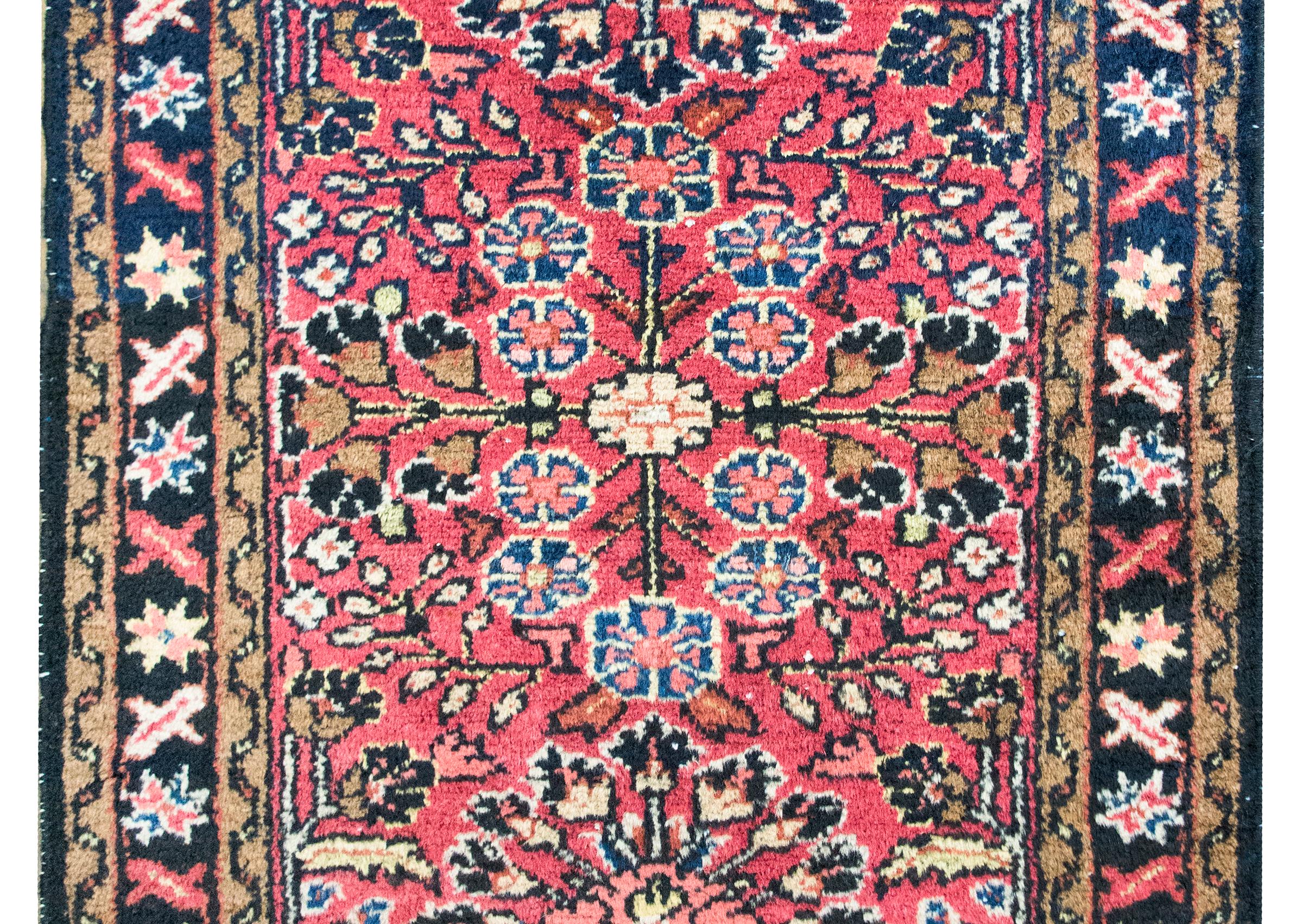 A charming petite early 20th century Persian Lilihan rug with a mirrored floral pattern with myriad floral clusters set against a coral background, surrounded by a simple stylized repeated floral patterned border, and all woven in indigo, pink,
