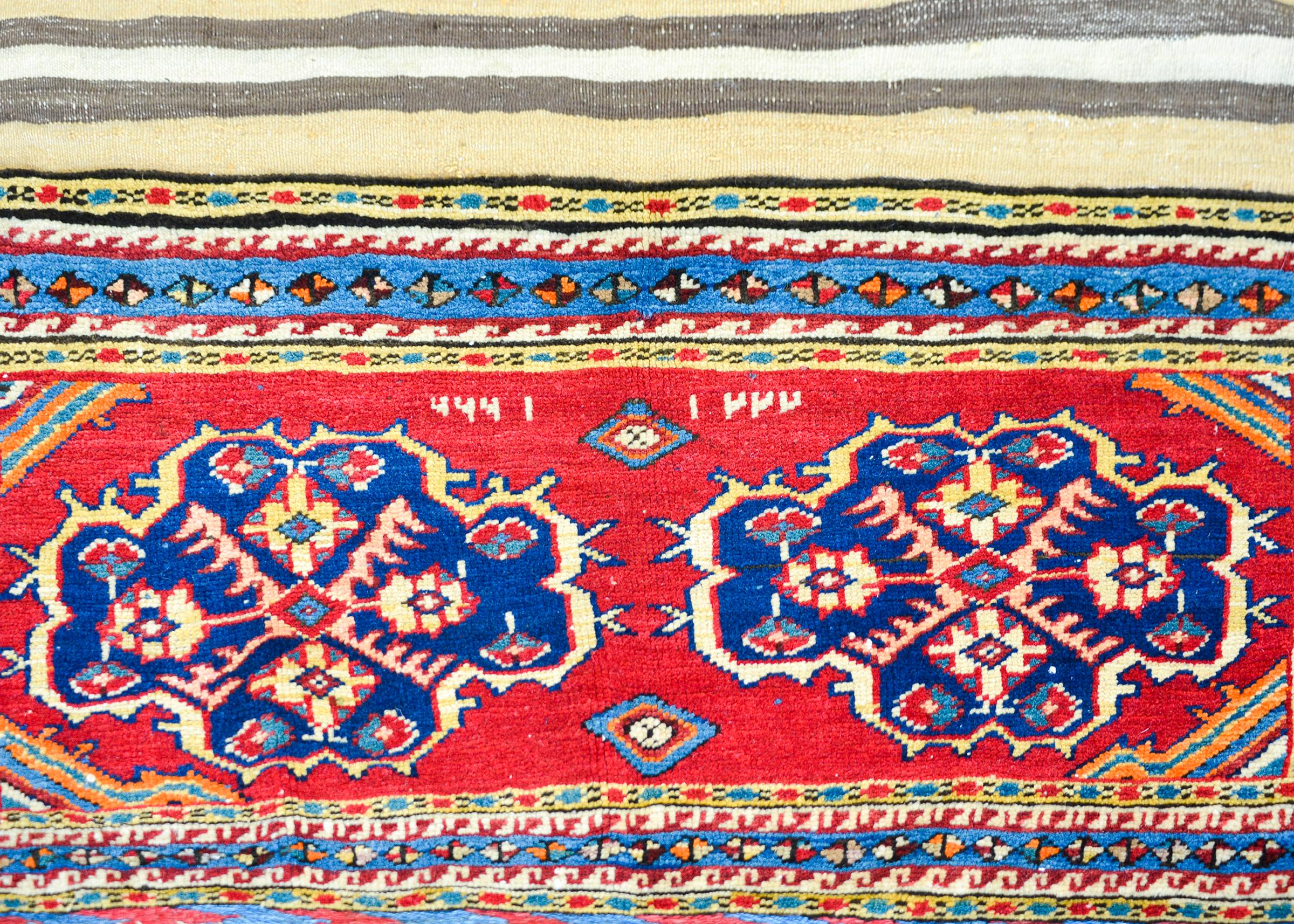 A stunning early 20th century Persian Lori horse blanket rug with ends woven with two floral medallions woven in indigo, crimson, and gold, and surrounded by petite geometric patterned strips, and connected with a simple striped flatweave backing.