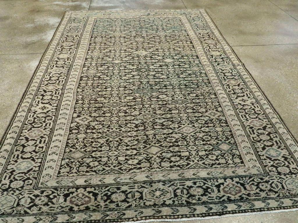Un antico tappeto d'accento persiano Malayer. Il fondo in carboncino presenta un motivo Herati allover con losanghe piene di colore invece dei soliti contorni. Il bordo abraso, prevalentemente marrone-nero, è in stile palmetta di tartaruga