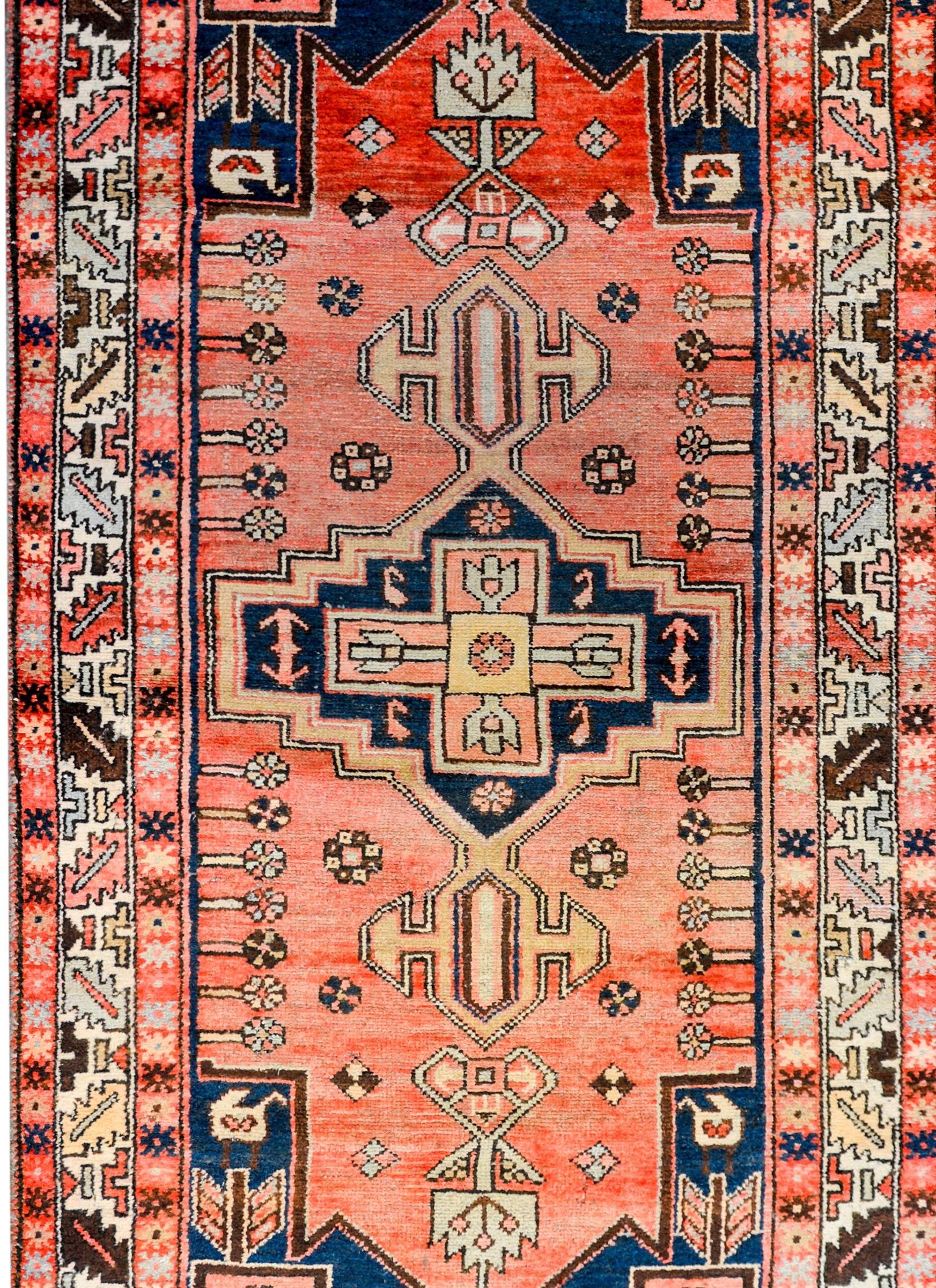 A beautiful early 20th century Persian Malayer rug with a bold tribal pattern woven with stylized floral forms woven in varying shades of crimson, light and dark indigo, natural undyed wool all on a abrash crimson background. The border is complex