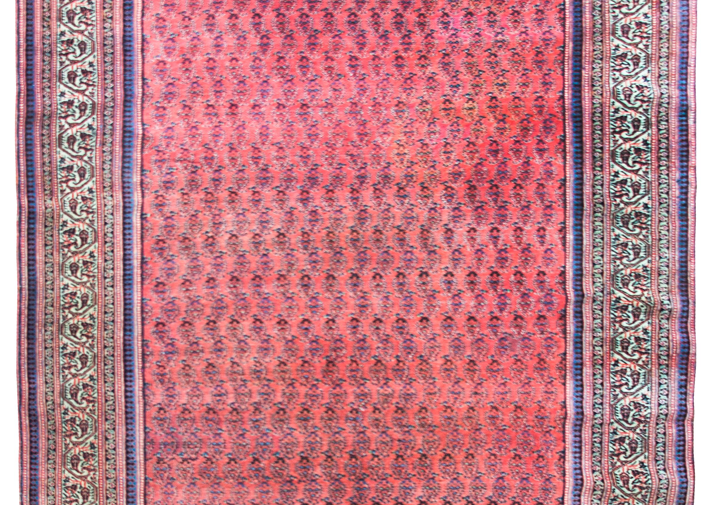 A beautiful early 20th century Persian Malayer with an all-over petite paisley pattern woven in varying shade of indigo, crimson, and pink, set over a crimson background, and all surrounded by a wide complex border with a wide central floral,