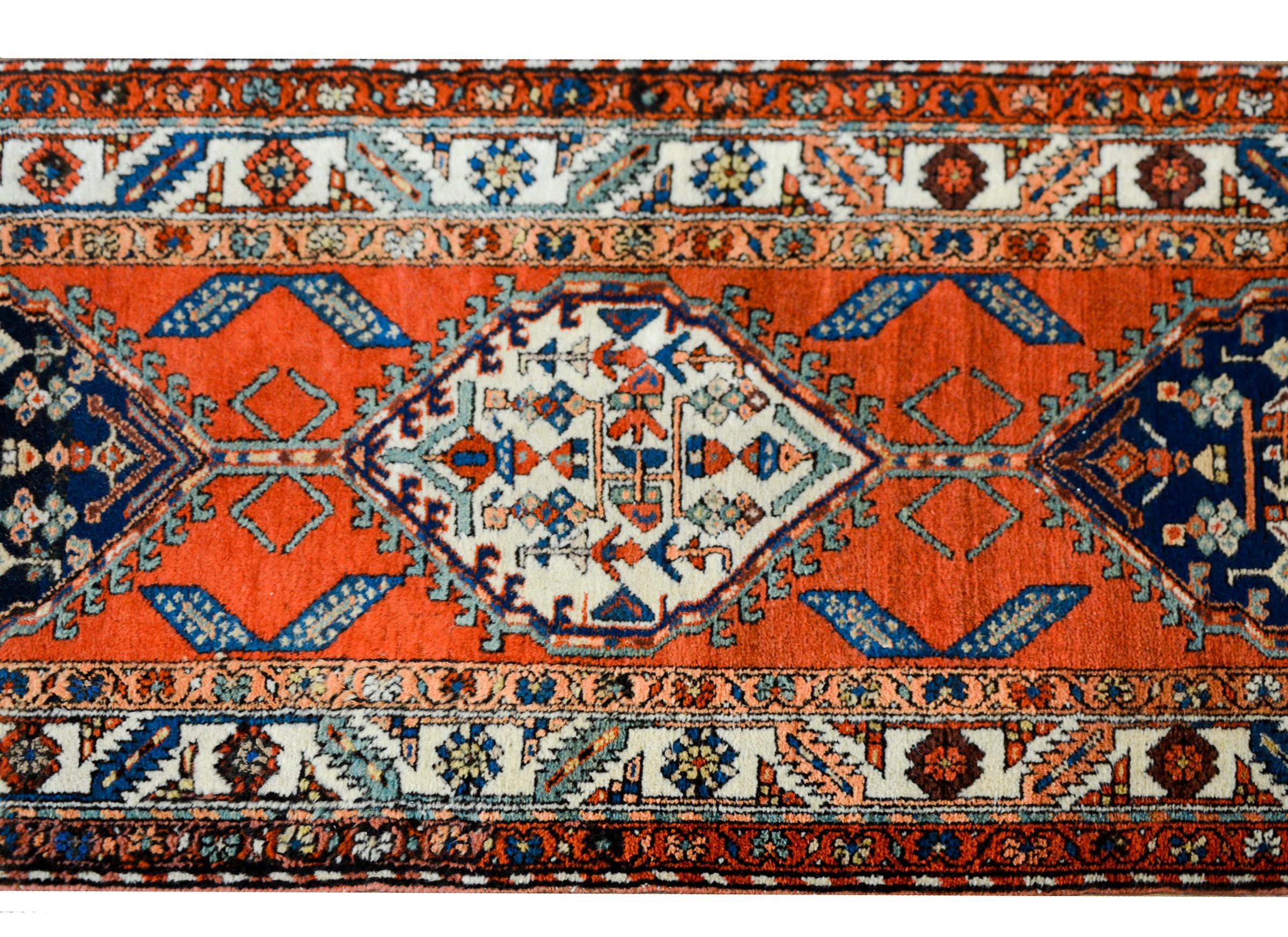 A bold early 20th century Persian Malayer runner with several diamond medallions against a crimson background and surrounded by a wonderful border with more stylized flowers and leaves, all woven in light and dark indigo, white, crimson, and gold.