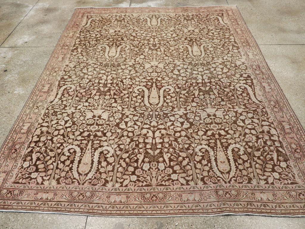 Una antigua alfombra persa Mashad de acento. El campo marrón Siena presenta cuatro hileras desplazadas de cipreses entrelazados por hojas dentadas recurvadas, todo ello dentro de un relleno de fondo muy denso de milhojas. Los bordes en retroceso son