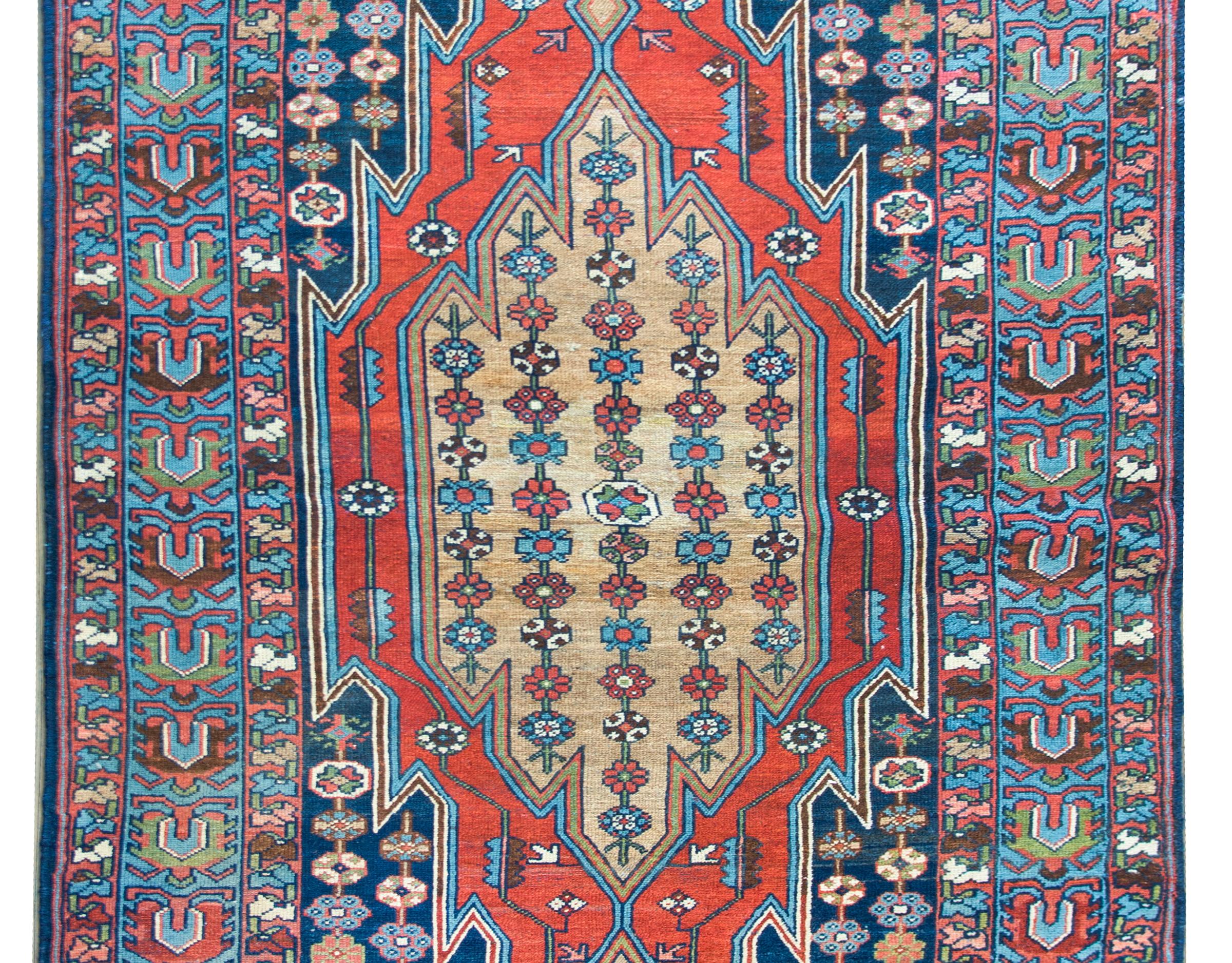 A beautiful early 20th century Persian Mazleghan rug with a large central medallion with flowers arranged in stripes, living amidst a field of even more flower, and surrounded by a wide border with a wide central stripe with stylized flowers flanked