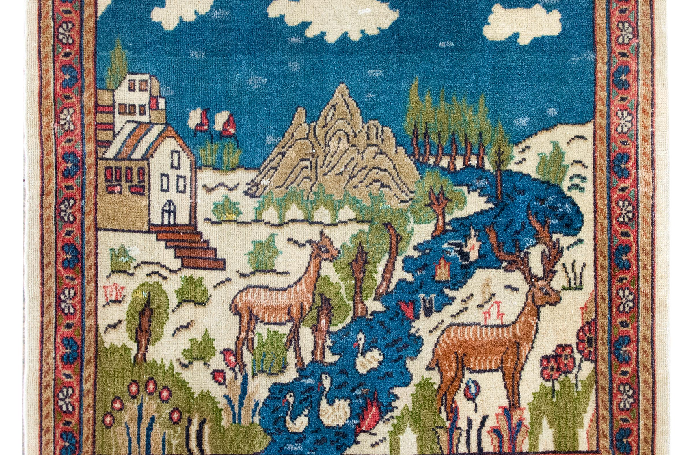 Un incantevole tappeto Tabriz pittorico persiano dell'inizio del XX secolo che raffigura due cervi in piedi sul bordo di un fiume con anatre che galleggiano.  Una casa in lontananza si trova dietro a una grande montagna e a una flora ricca di alberi