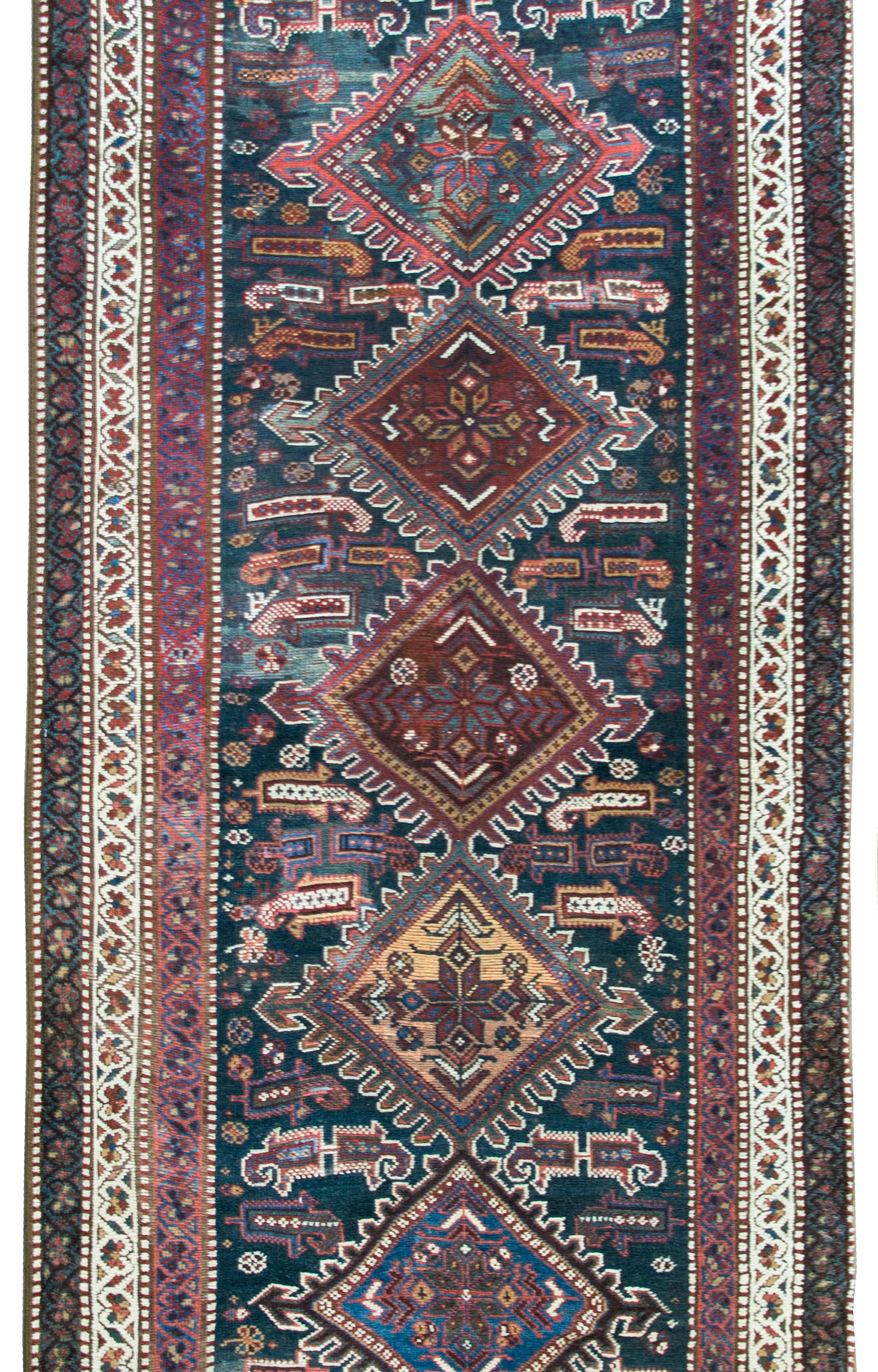 A beautiful early 20th century Persian Qashqai runner with the most wonderful tribal pattern with seven large diamond medallions, each woven with stylized flowers, and living amidst a field of stylized paisley patterns, surrounded by a border