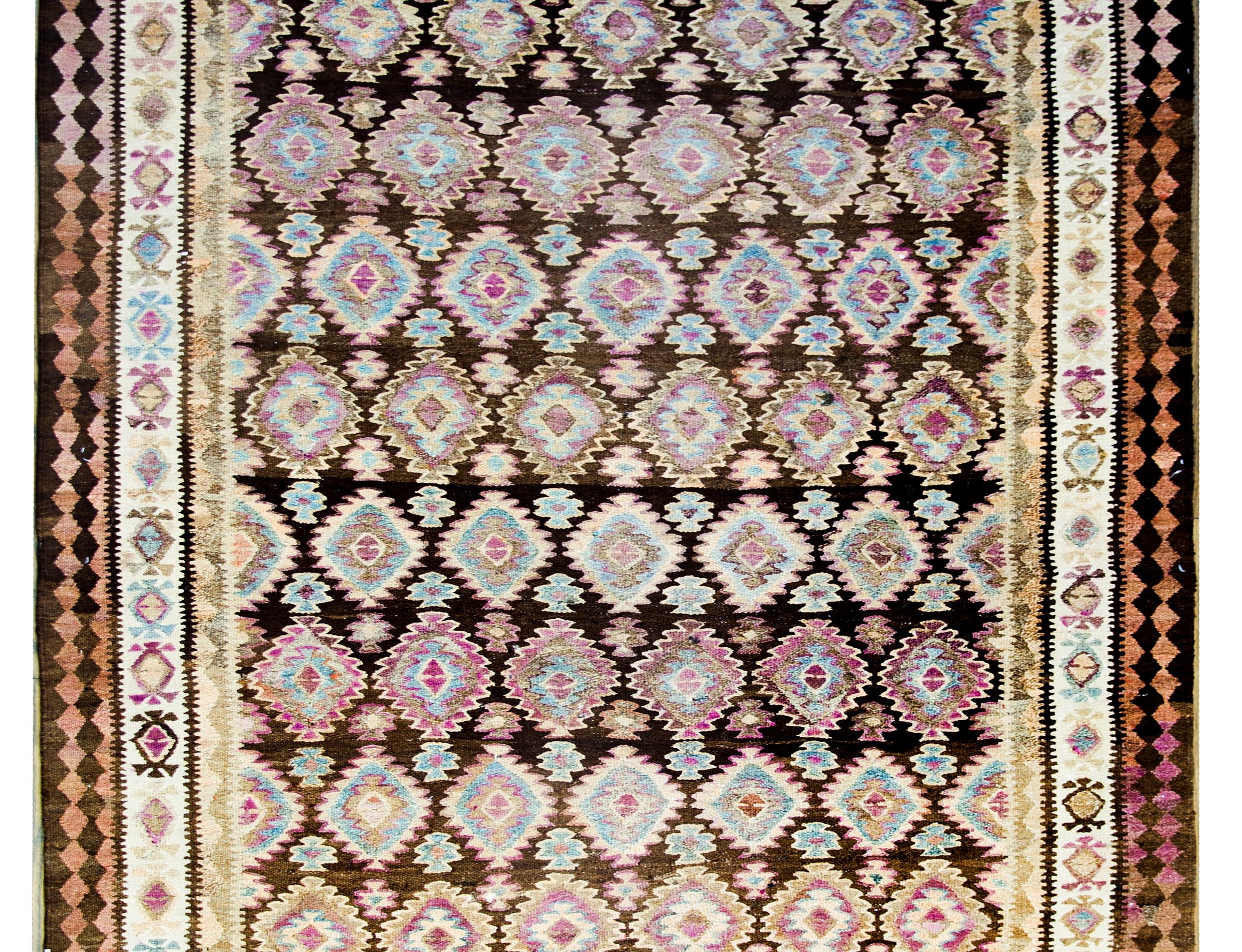 Ein persischer Qazvin-Kelim-Teppich aus dem frühen 20. Jahrhundert mit einem Allover-Rautenmuster aus mehrfarbiger Wolle, umgeben von einer komplexen Bordüre aus geometrisch gemusterten Streifen.