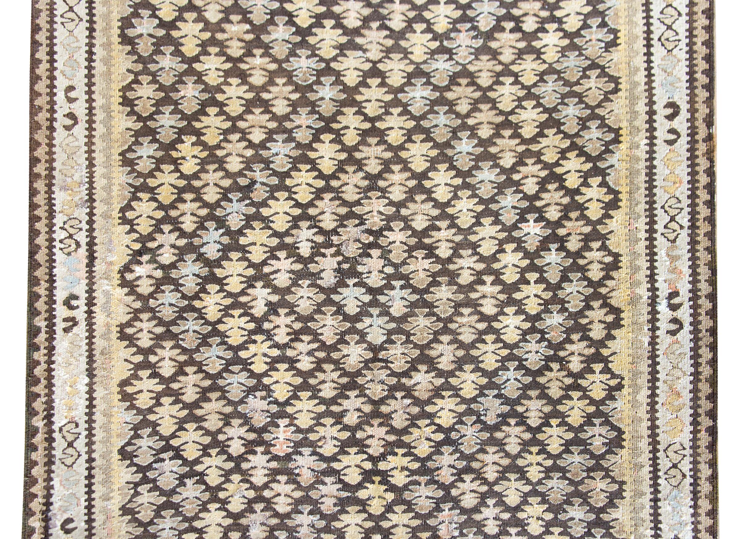 A wonderful early 20th century Persian Qazvin kilim rug with an all-over tree-of-life pattern woven with varying colored stripes creating a zigzag pattern across the field, and surrounded by several geometric patterned stripes.