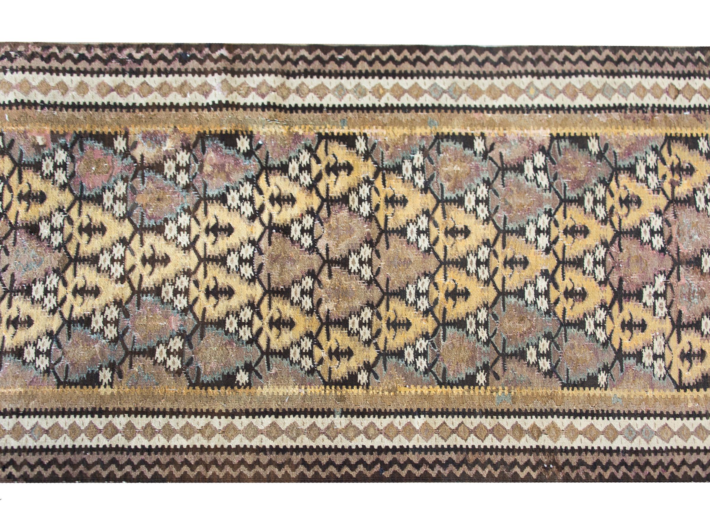 A beautiful early 20th century Persian Qazvin kilim rug with an all-over tree-of-life pattern woven in muted golds, violets, indigos, and natural browns and whites, and surrounded by a border composed of multiple petite geometric patterned stripes.