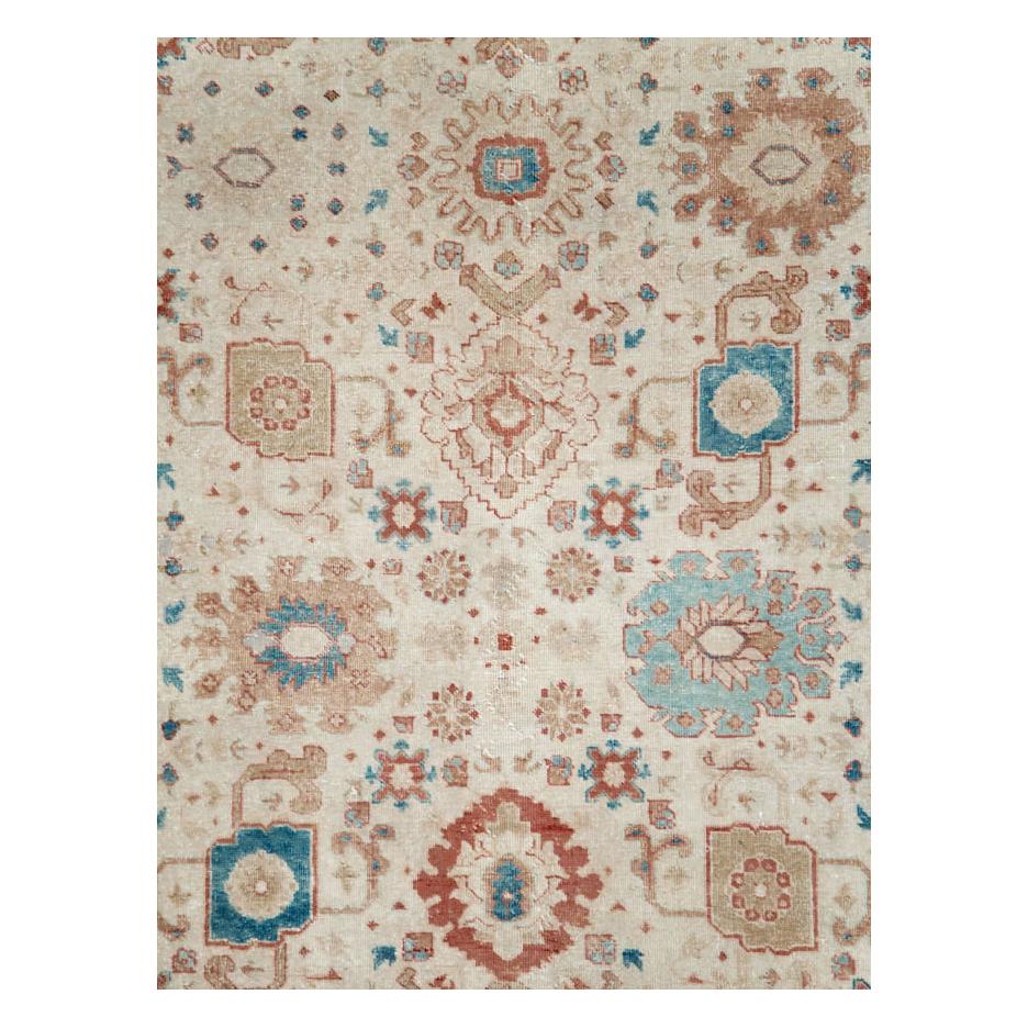 An antique Persian Tabriz room size carpet handmade during the early 20th century. The cream field is decorated by semi-geometric floral elements including classic 'Harshang' palmettes in shades of brick red and bluish-green (aqua), and enclosed by